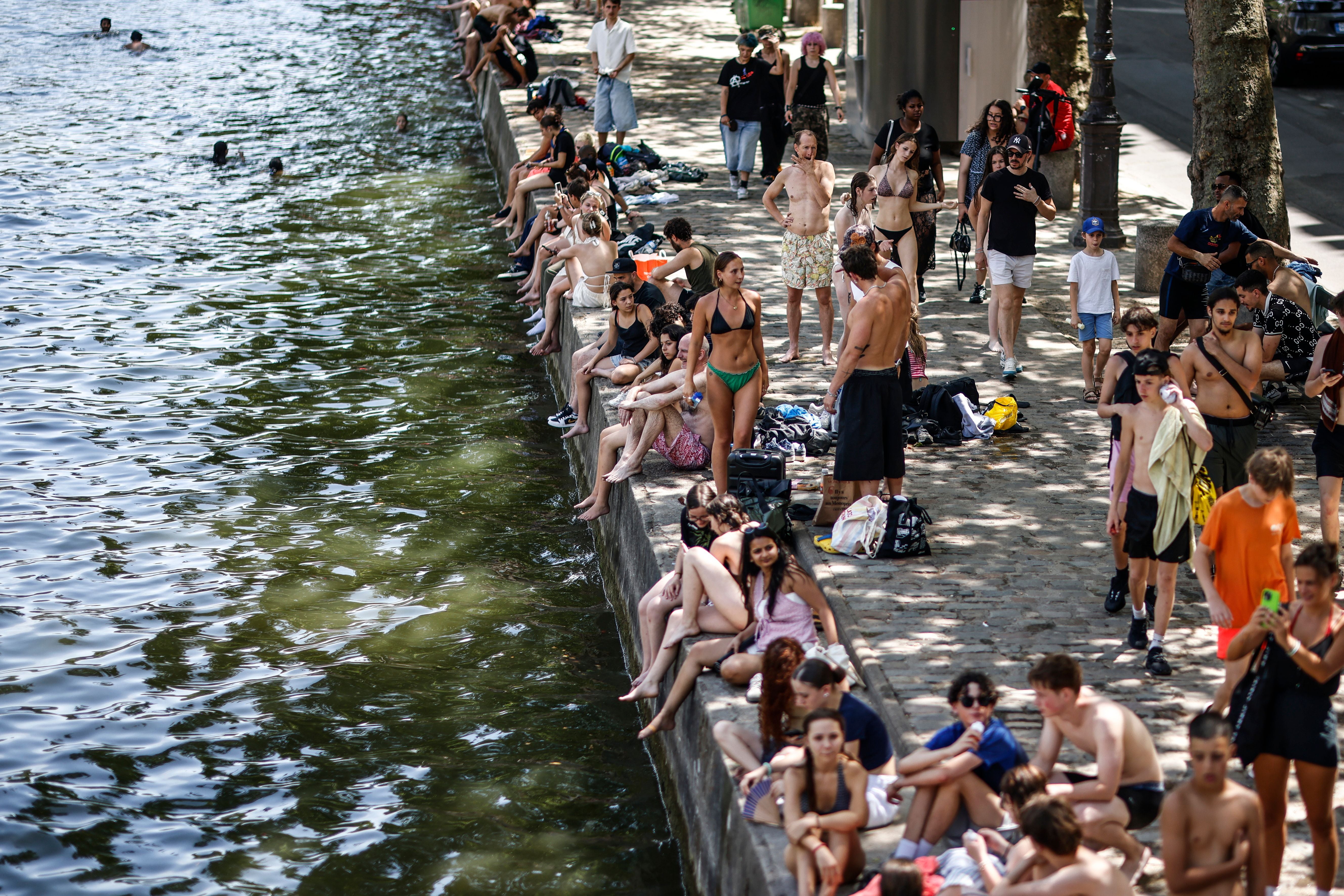 Viele Menschen sitzen und stehen in Badekleidung am Ufer des Canal Saint-Martin in Paris.