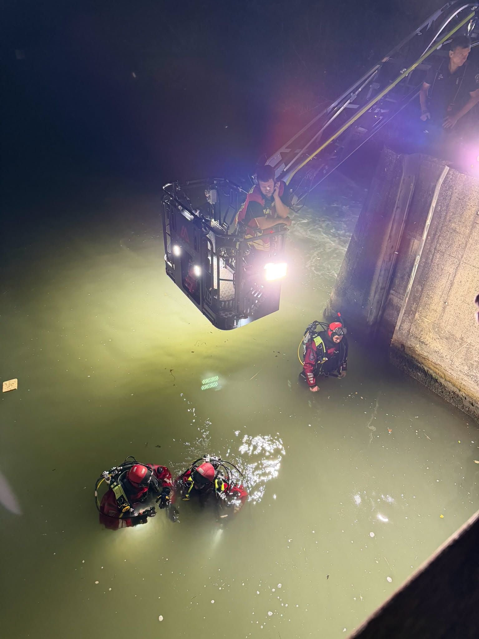 Zwei Feuerwehrtaucher im Wasser bei Nacht, Korb einer Drehleiter leuchtet Szene aus.