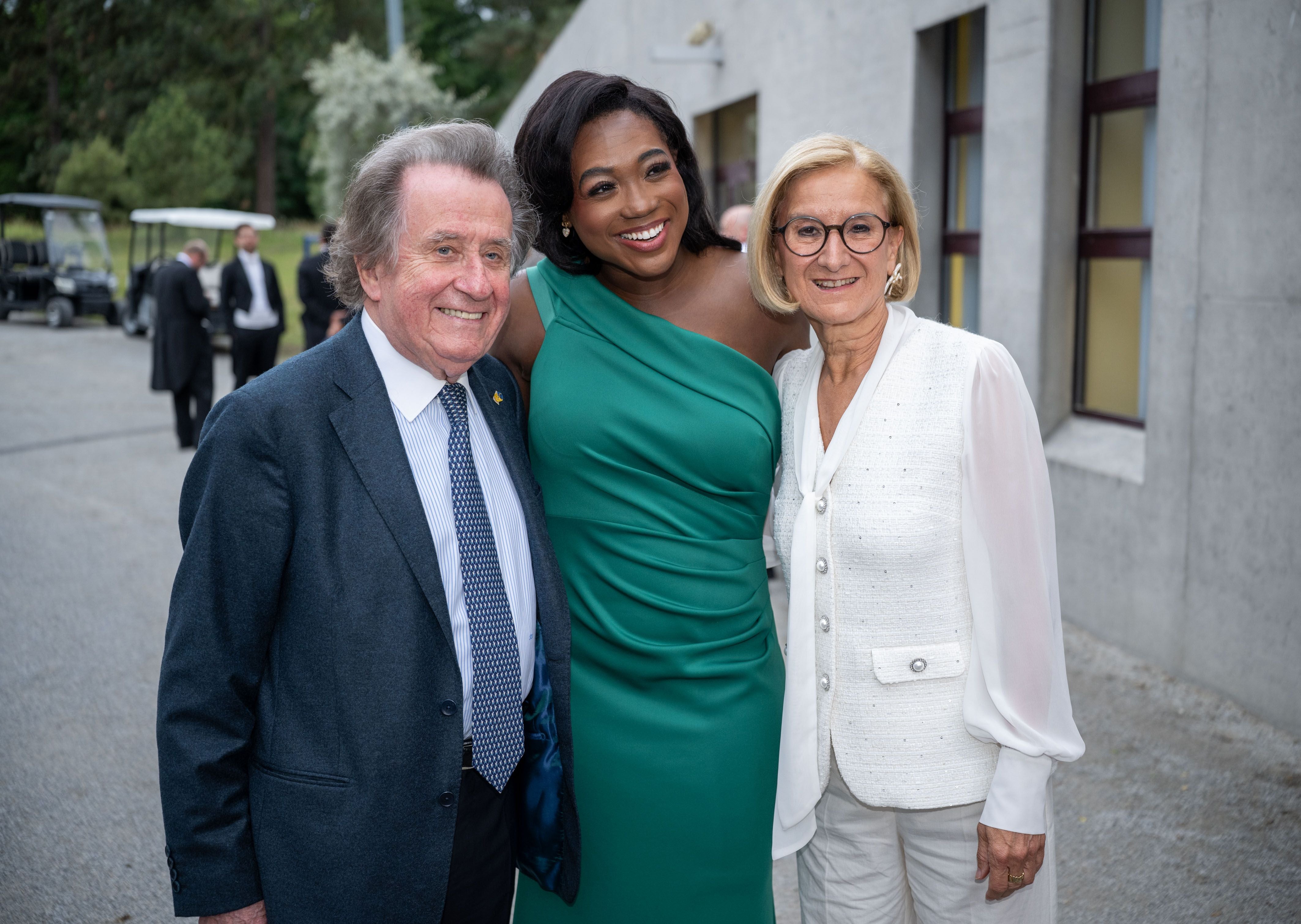 Drei Personen posieren elegant gekleidet für ein Foto im Freien vor einem Gebäude.