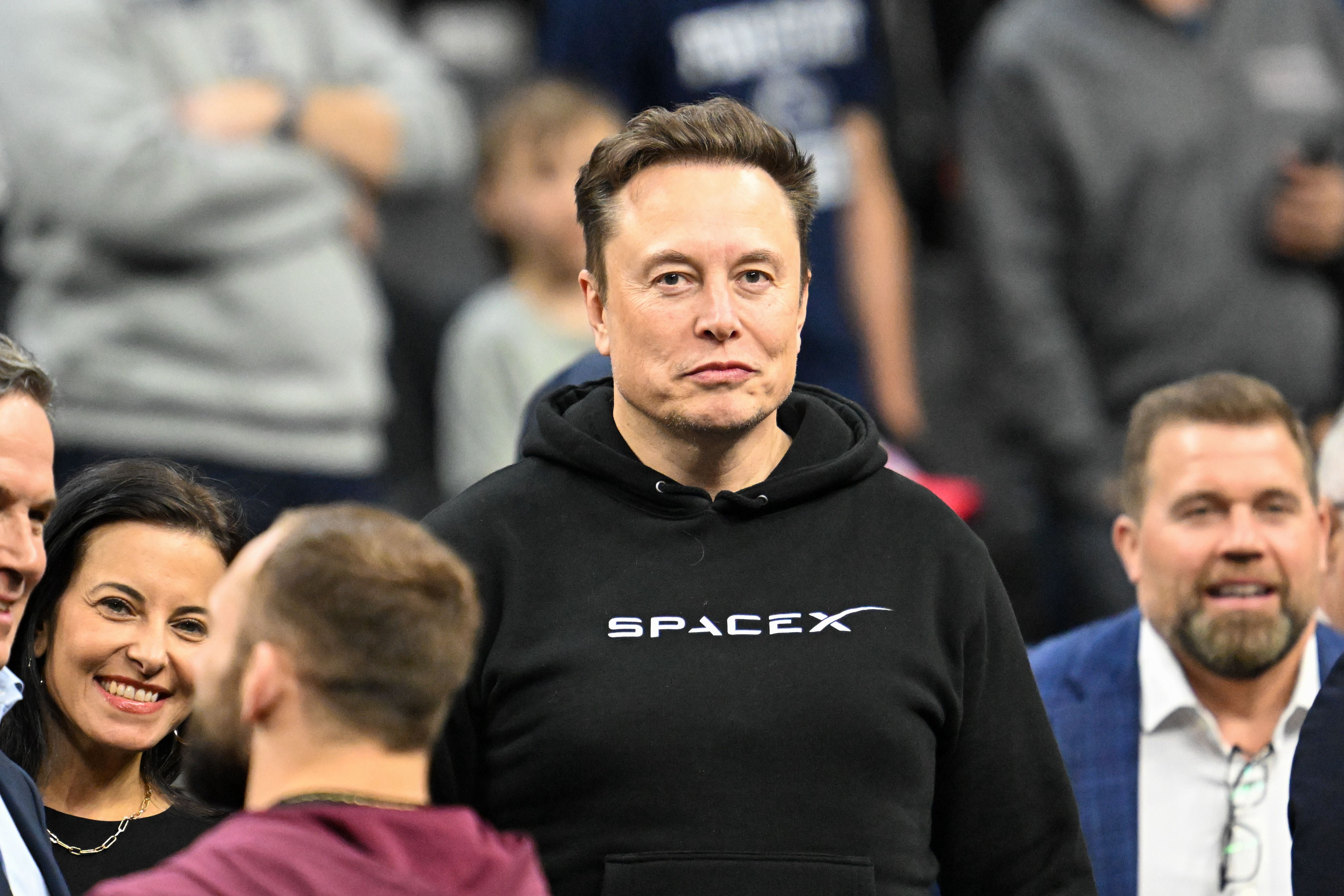 Eine Person trägt einen schwarzen SpaceX-Hoodie inmitten einer Menschenmenge bei einem Sportevent.