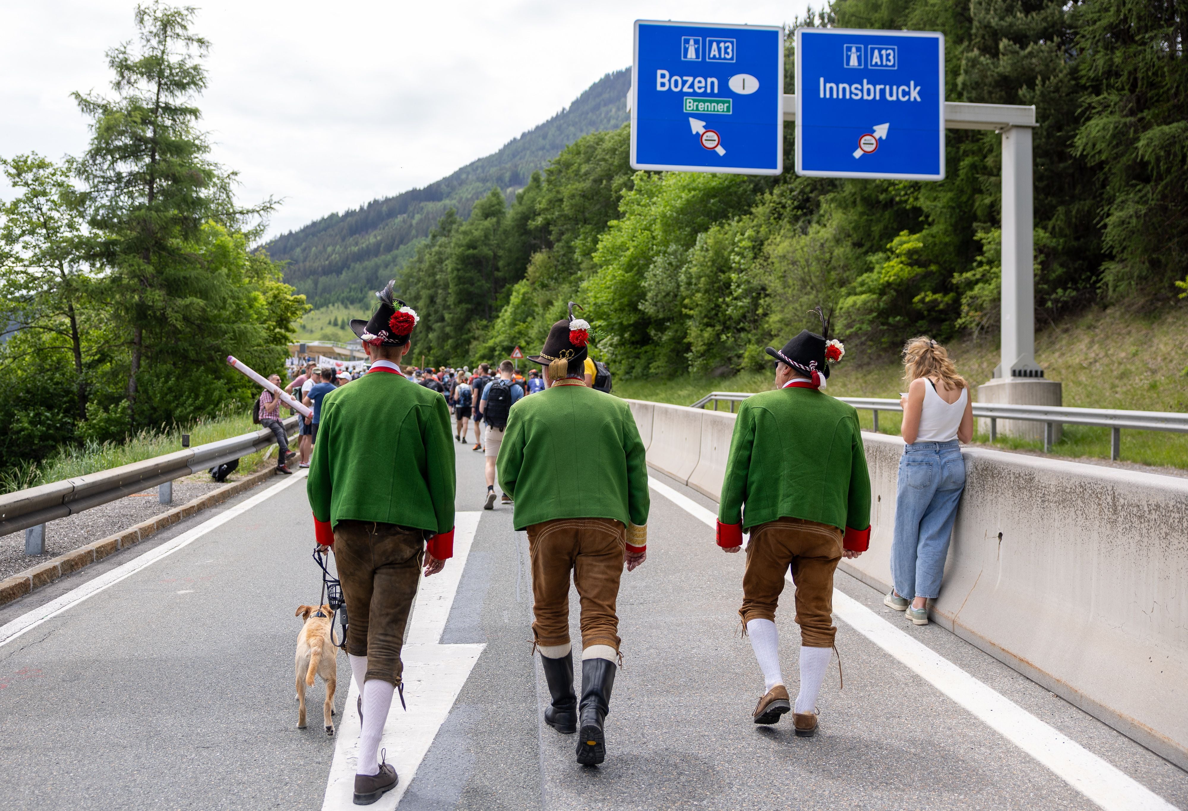 Drei Männer in Tiroler Tracht gehen mit einem Hund auf der gesperrten Brennerautobahn Richtung Bozen.