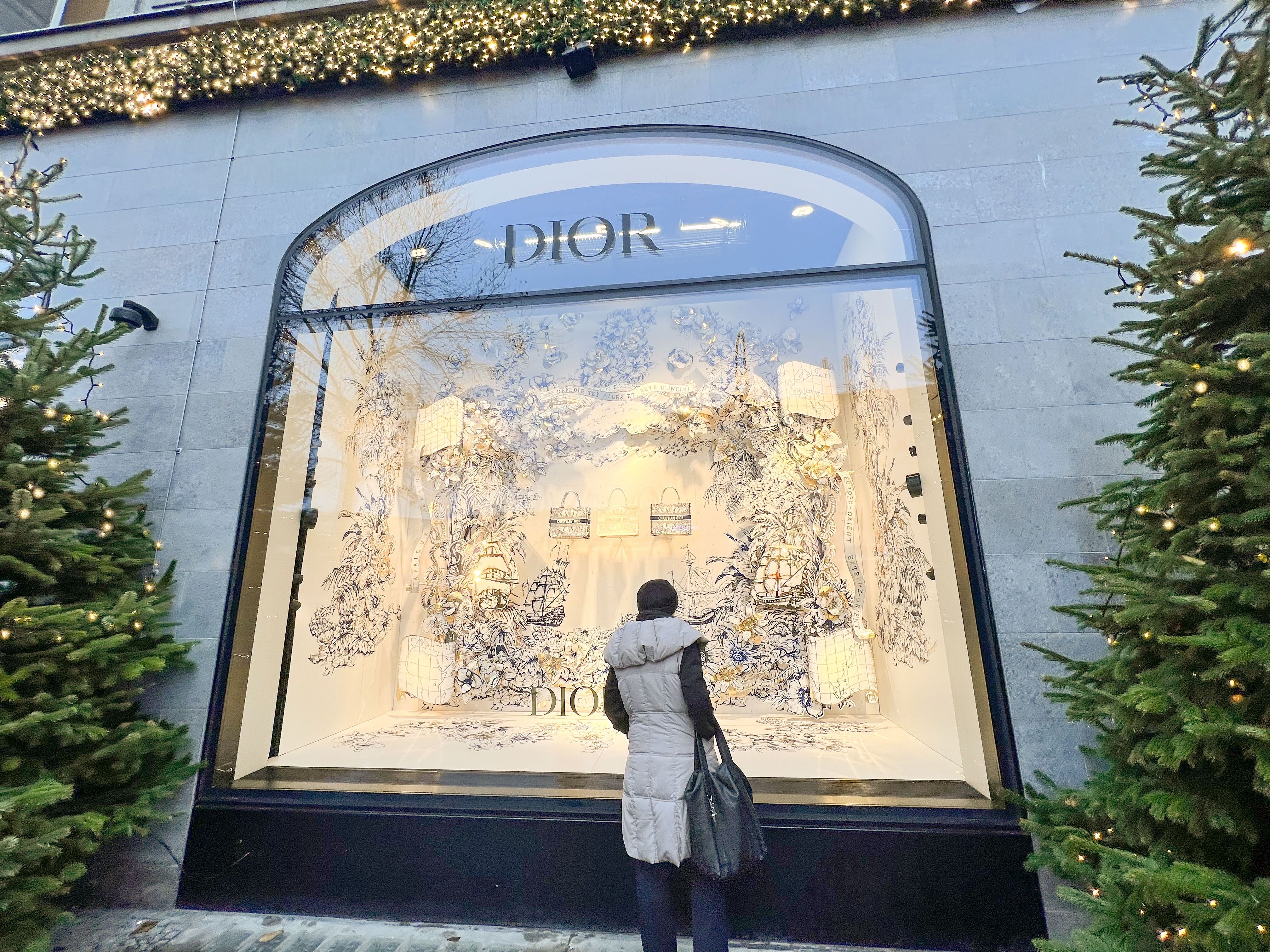 Eine Person betrachtet ein weihnachtlich dekoriertes Dior-Schaufenster im KaDeWe Berlin.
