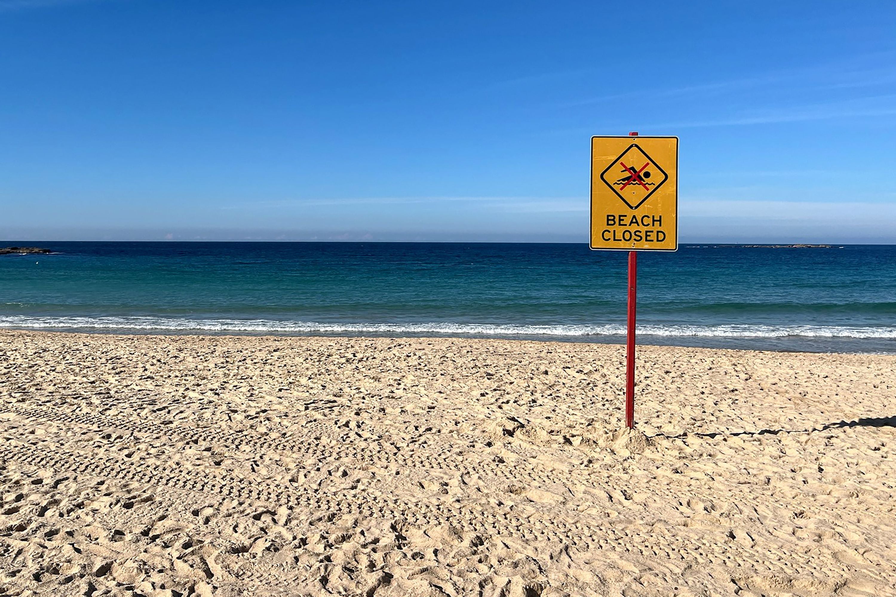 Strand mit Schild "Beach Closed" vor blauem Meer und klarem Himmel in Sydney, Australien.
