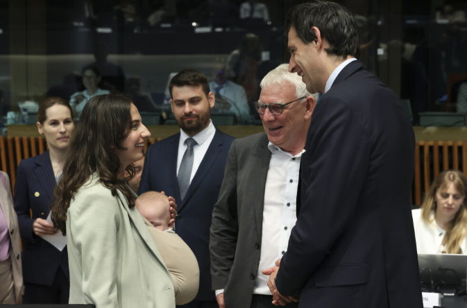 Eine Ministerin hält ein Baby und spricht im EU-Rat mit mehreren Anwesenden.
