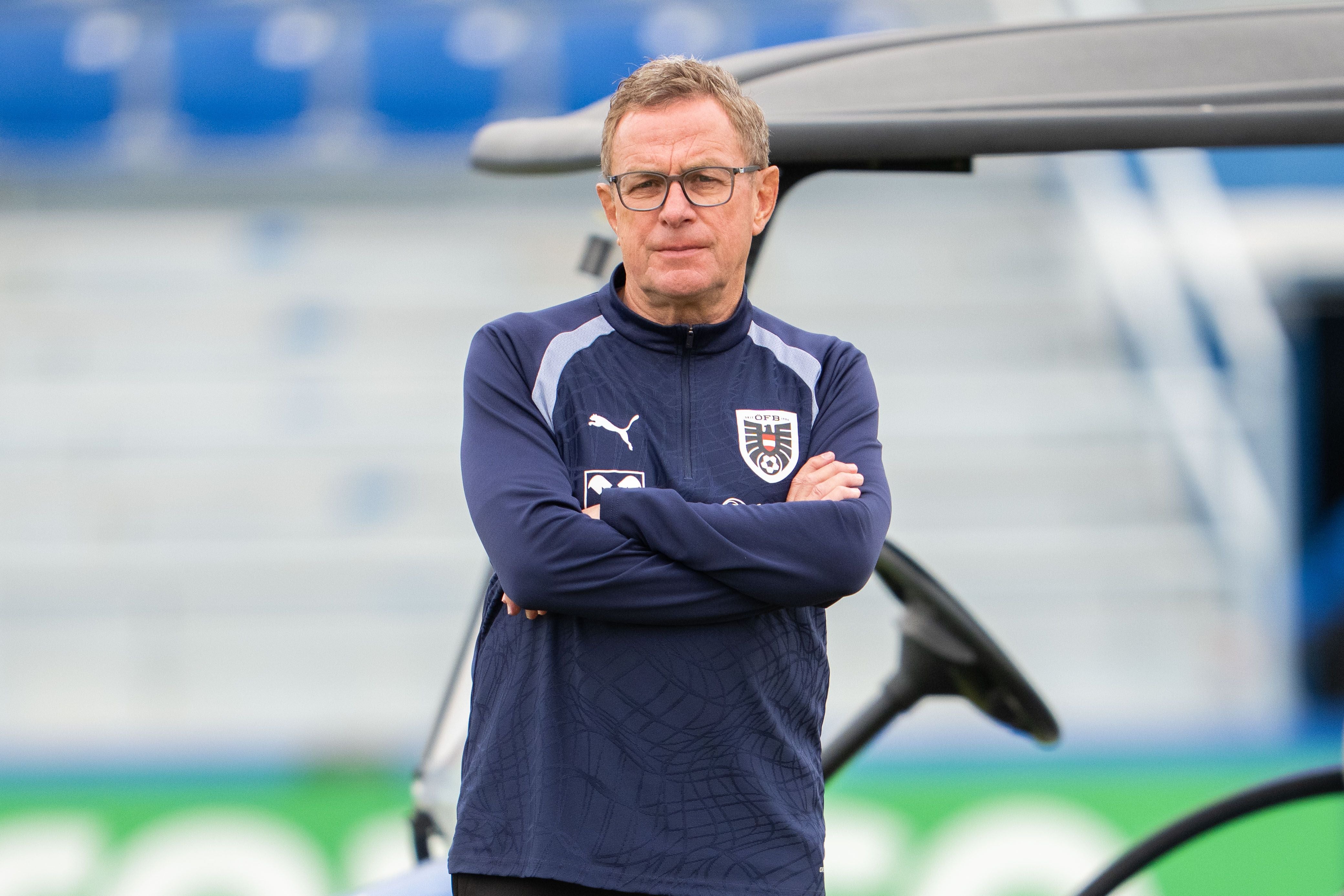 Ein Trainer im blauen ÖFB-Trainingsanzug steht mit verschränkten Armen auf einem Sportplatz.