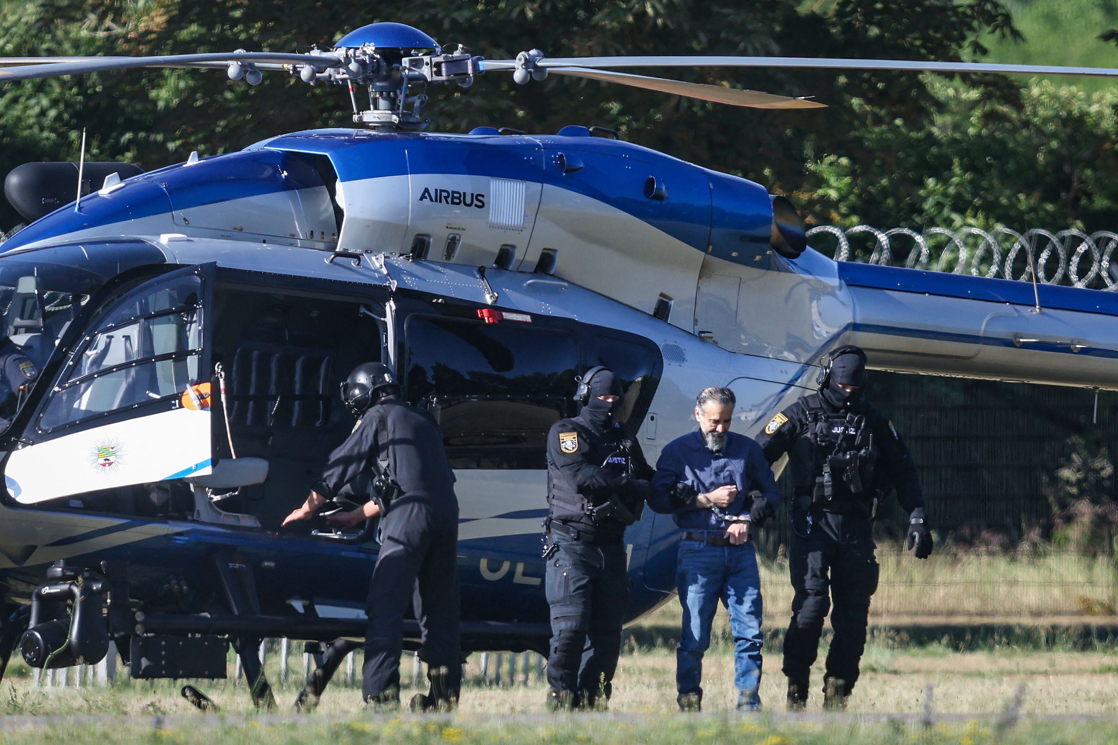 Bewaffnete Polizisten eskortieren einen Mann mit Handschellen aus einem Hubschrauber.