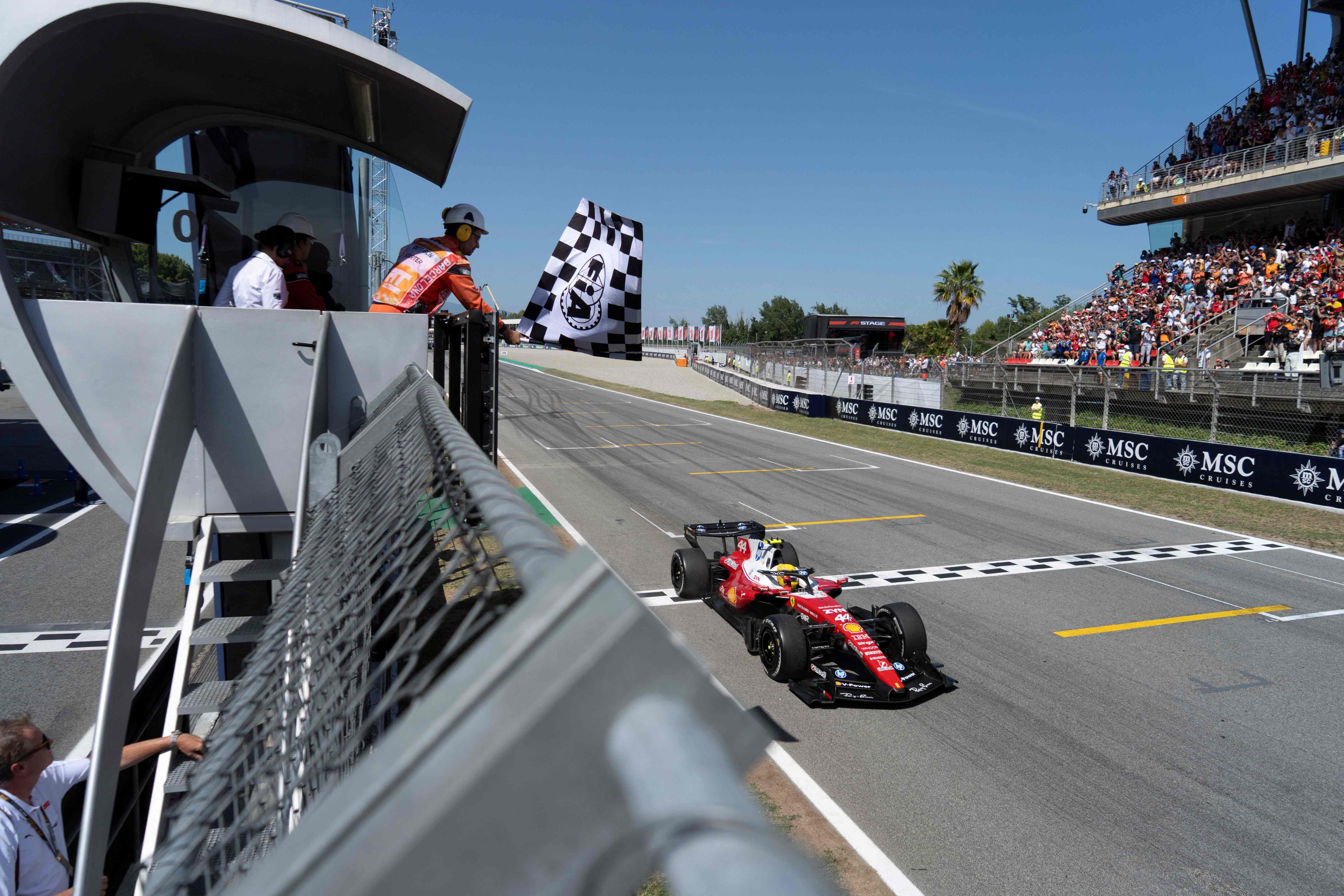 Ein rotes Ferrari-Formel-1-Auto überquert als Erster die Ziellinie, die Zielflagge wird geschwenkt.