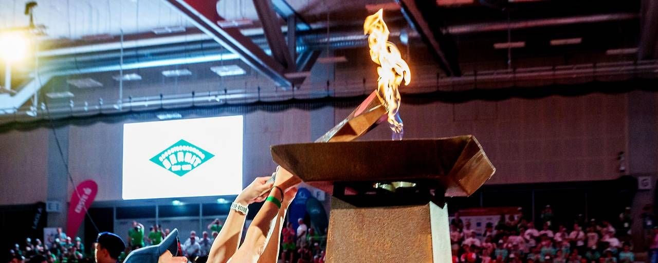 Menschen entzünden das Olympische Feuer bei einer Sportveranstaltung in einer Halle.