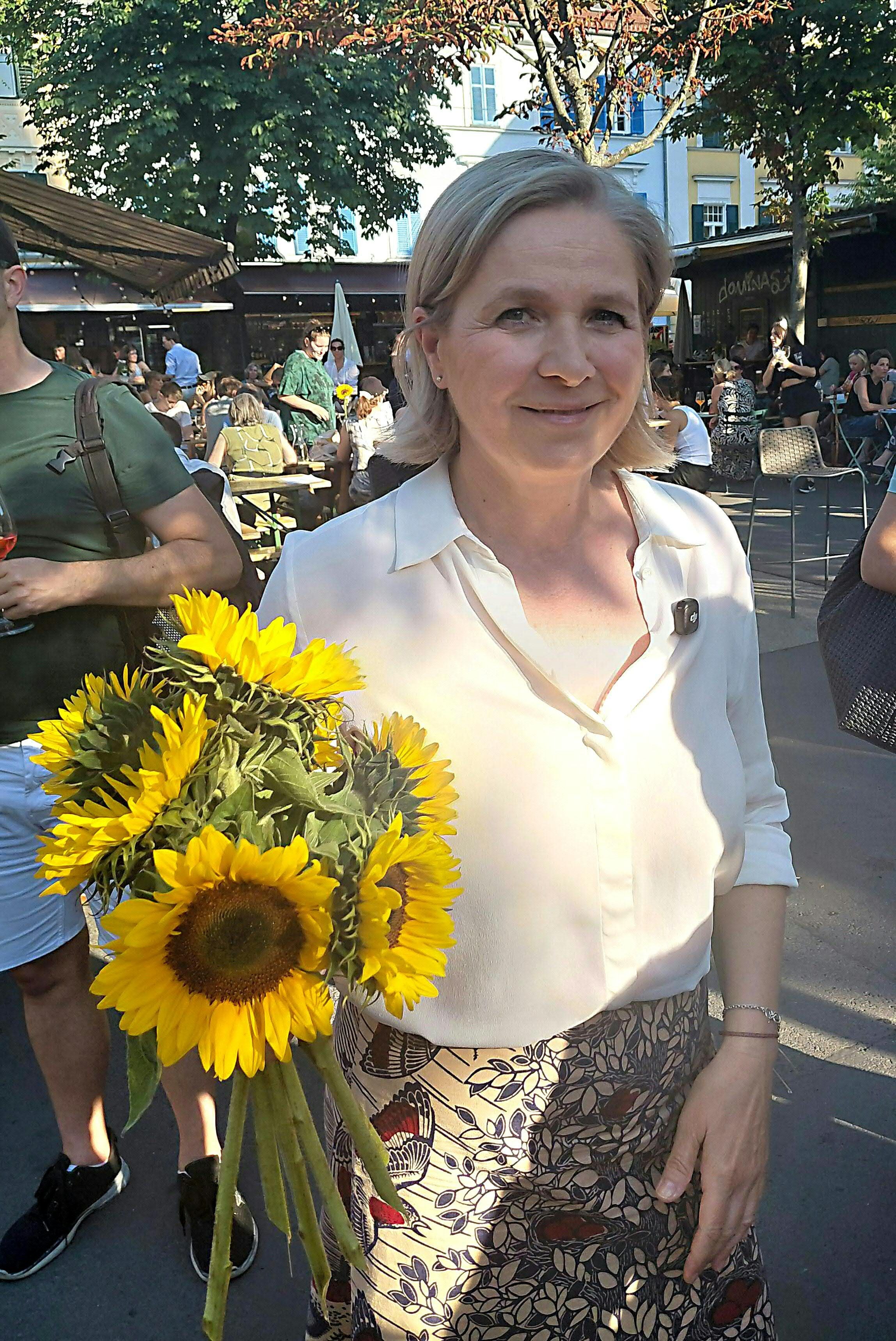 Eine Frau hält einen Strauß Sonnenblumen auf einer belebten Veranstaltung im Freien.