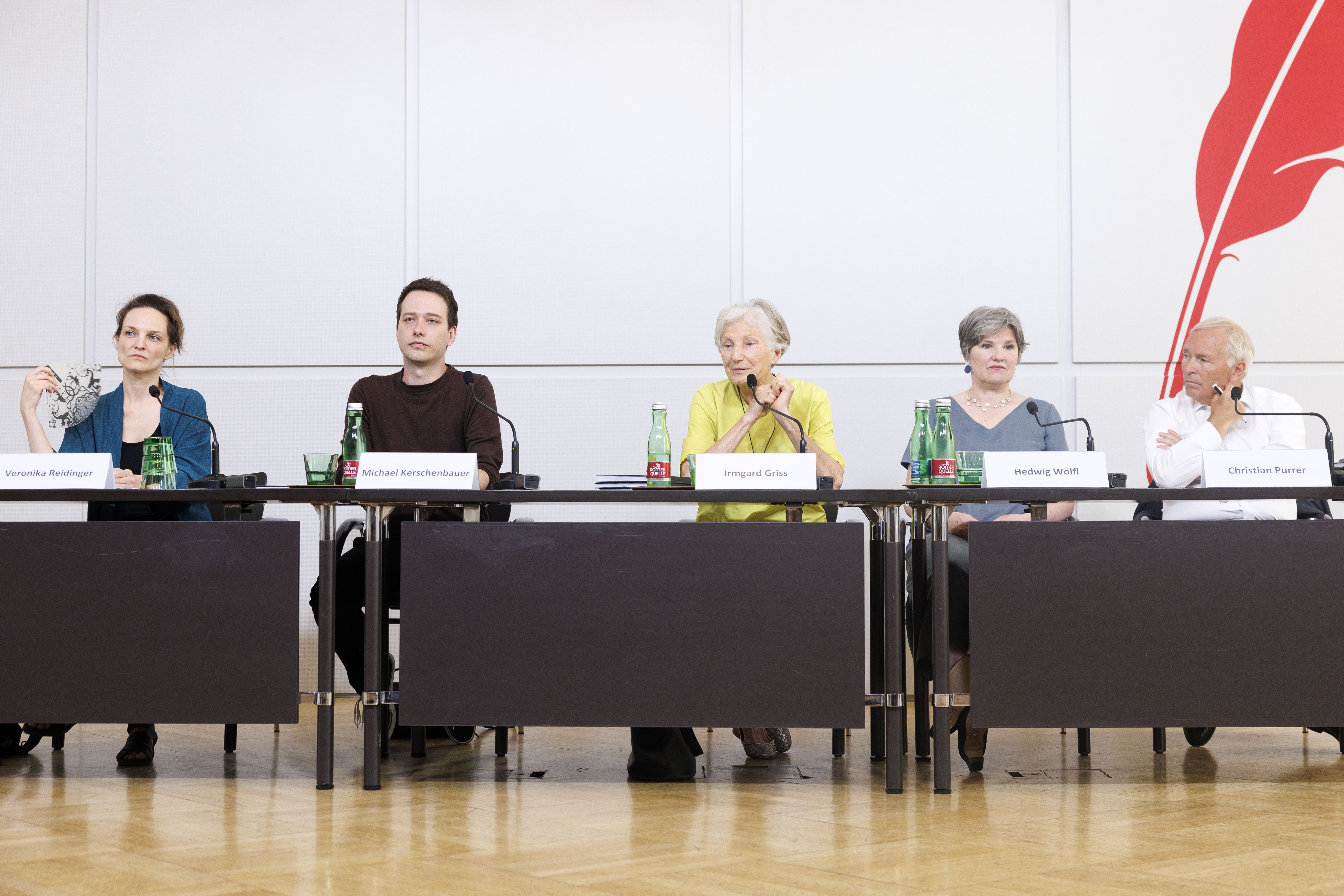 Fünf Personen sitzen bei einer Pressekonferenz an einem Tisch, vor ihnen stehen Namensschilder und Wasserflaschen.