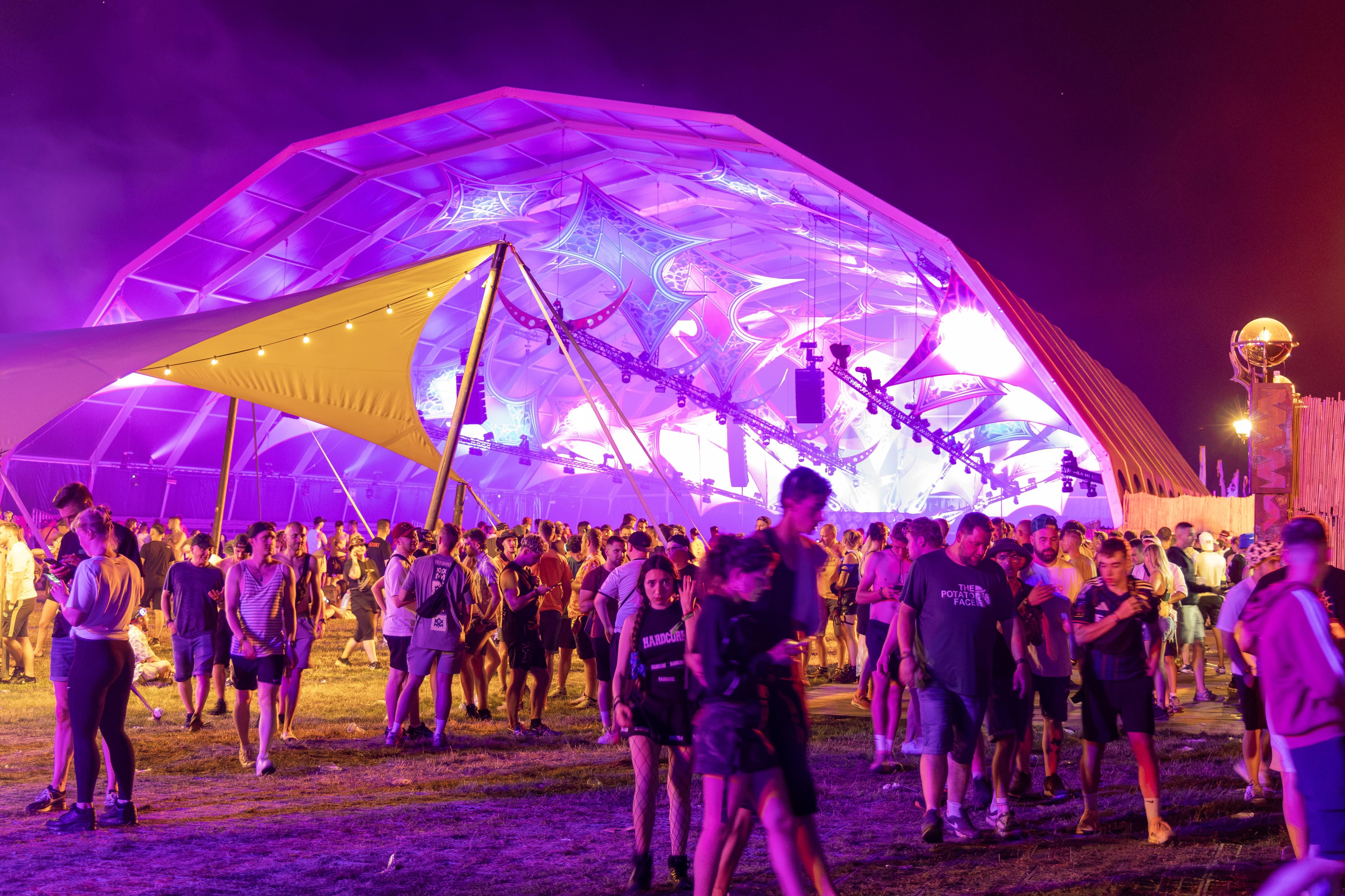 Viele Menschen stehen nachts bei lila Licht auf einem Festivalgelände mit futuristischer Bühne.