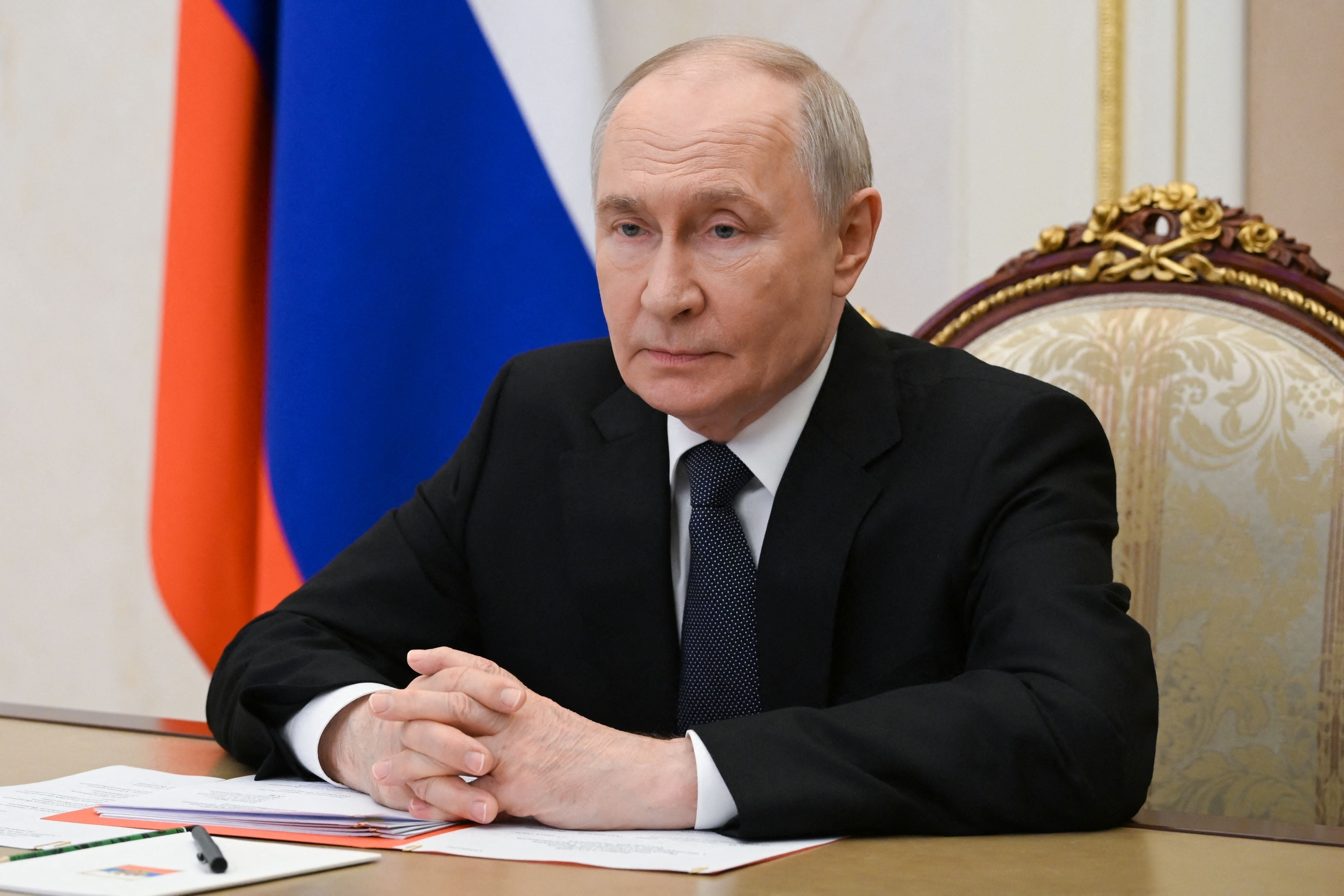 Ein Mann im Anzug sitzt an einem Tisch vor russischer Flagge, sein Gesicht ist verpixelt.