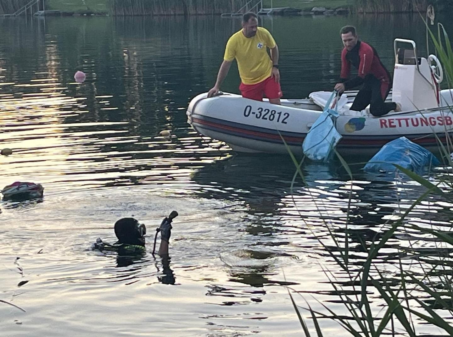Ein Taucher und zwei Rettungskräfte bergen Müll aus einem See mit einem Schlauchboot.