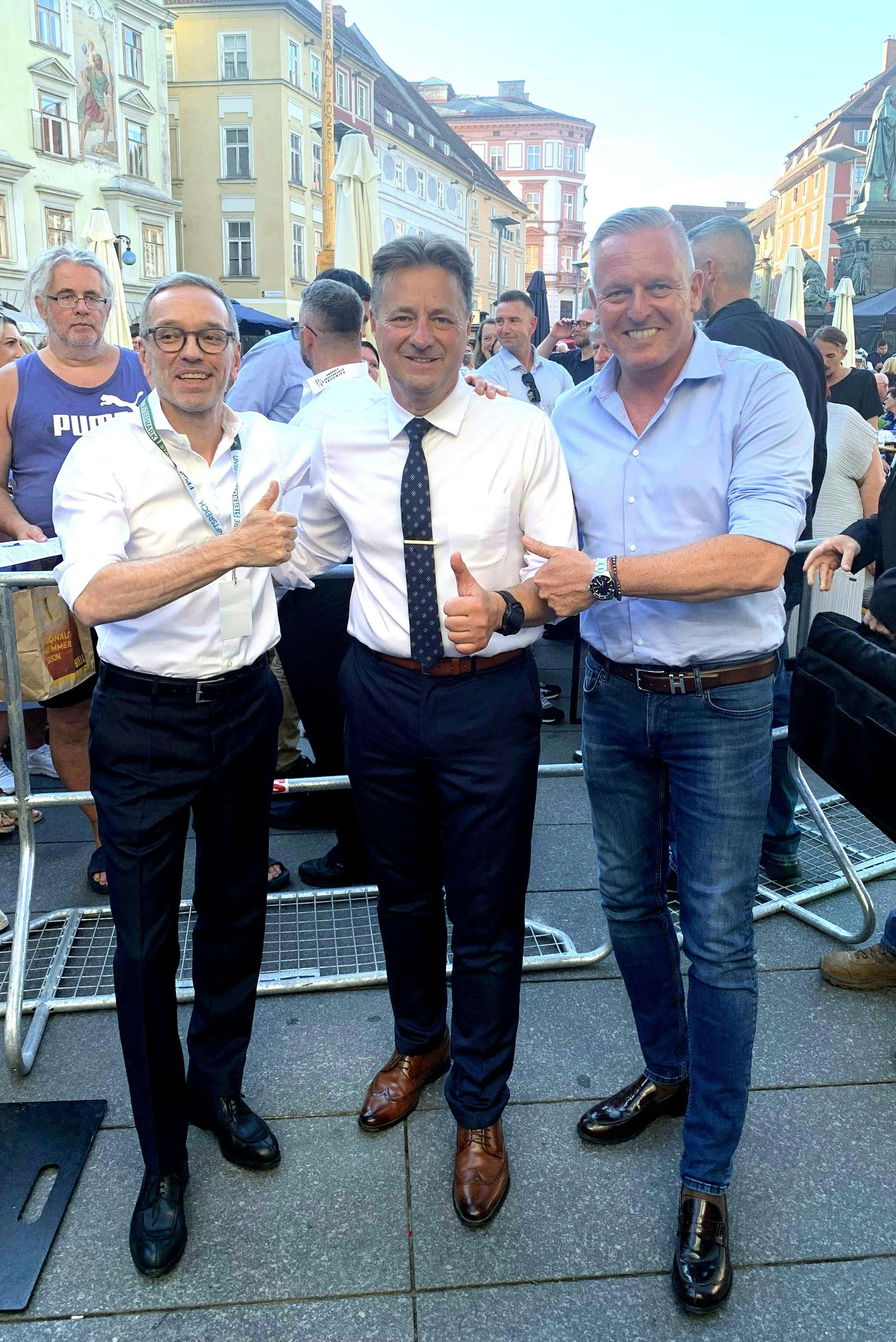 Drei Männer posieren bei einer Wahlkampfveranstaltung im Freien in Graz für ein Foto.