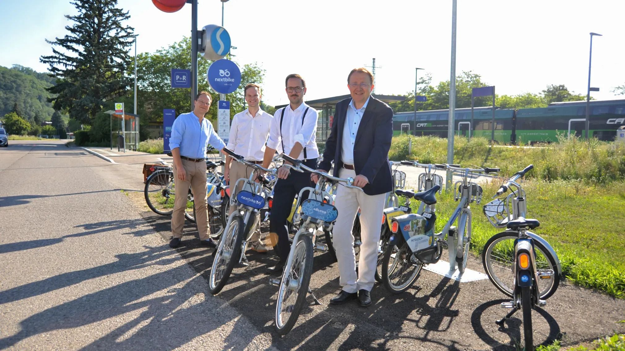 Vier Männer stehen bei einer Nextbike-Station mit Leihfahrrädern am Bahnhof Viehofen.