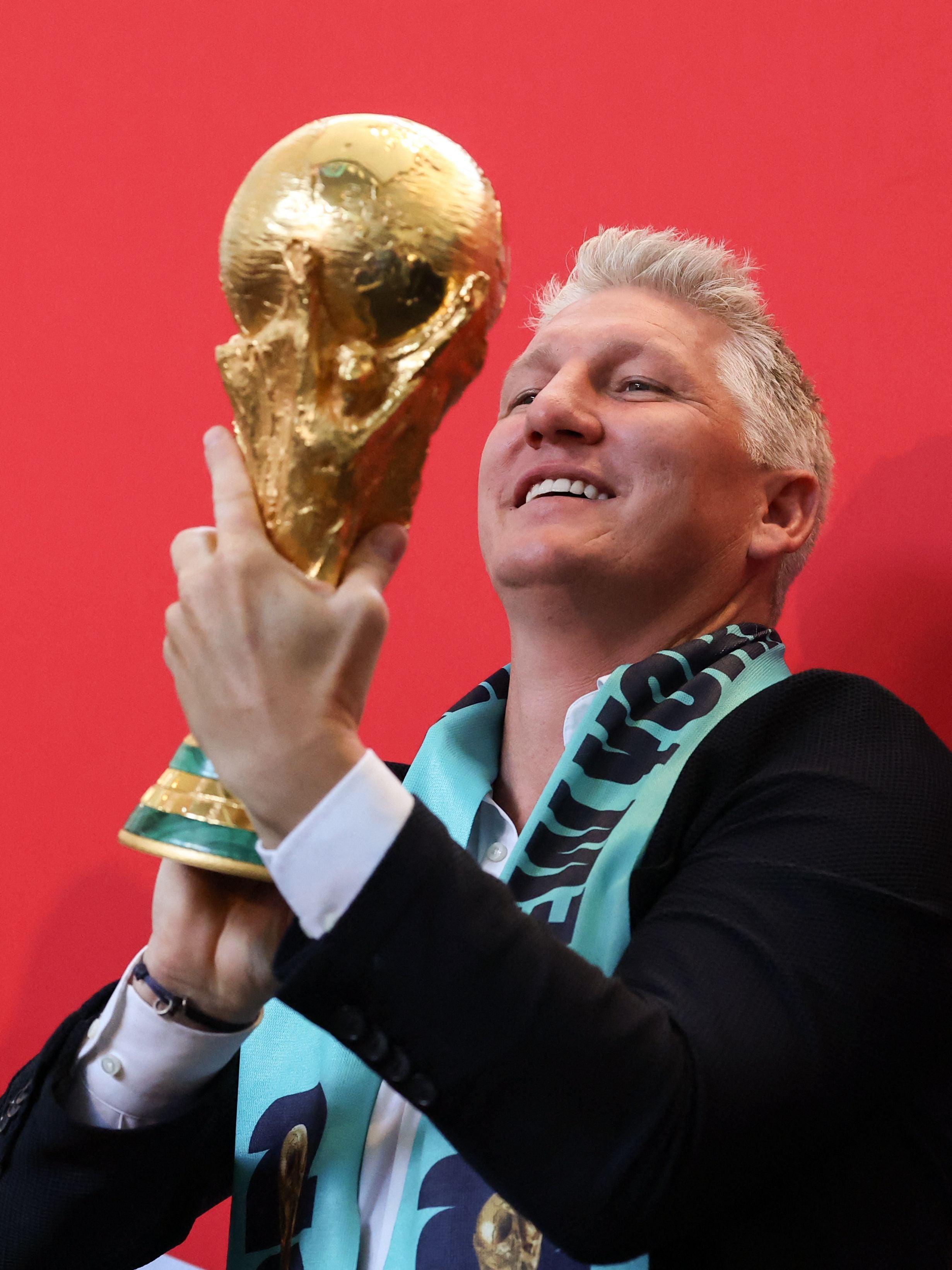 Eine Person hält den FIFA-Weltpokal vor rotem Hintergrund in die Höhe.