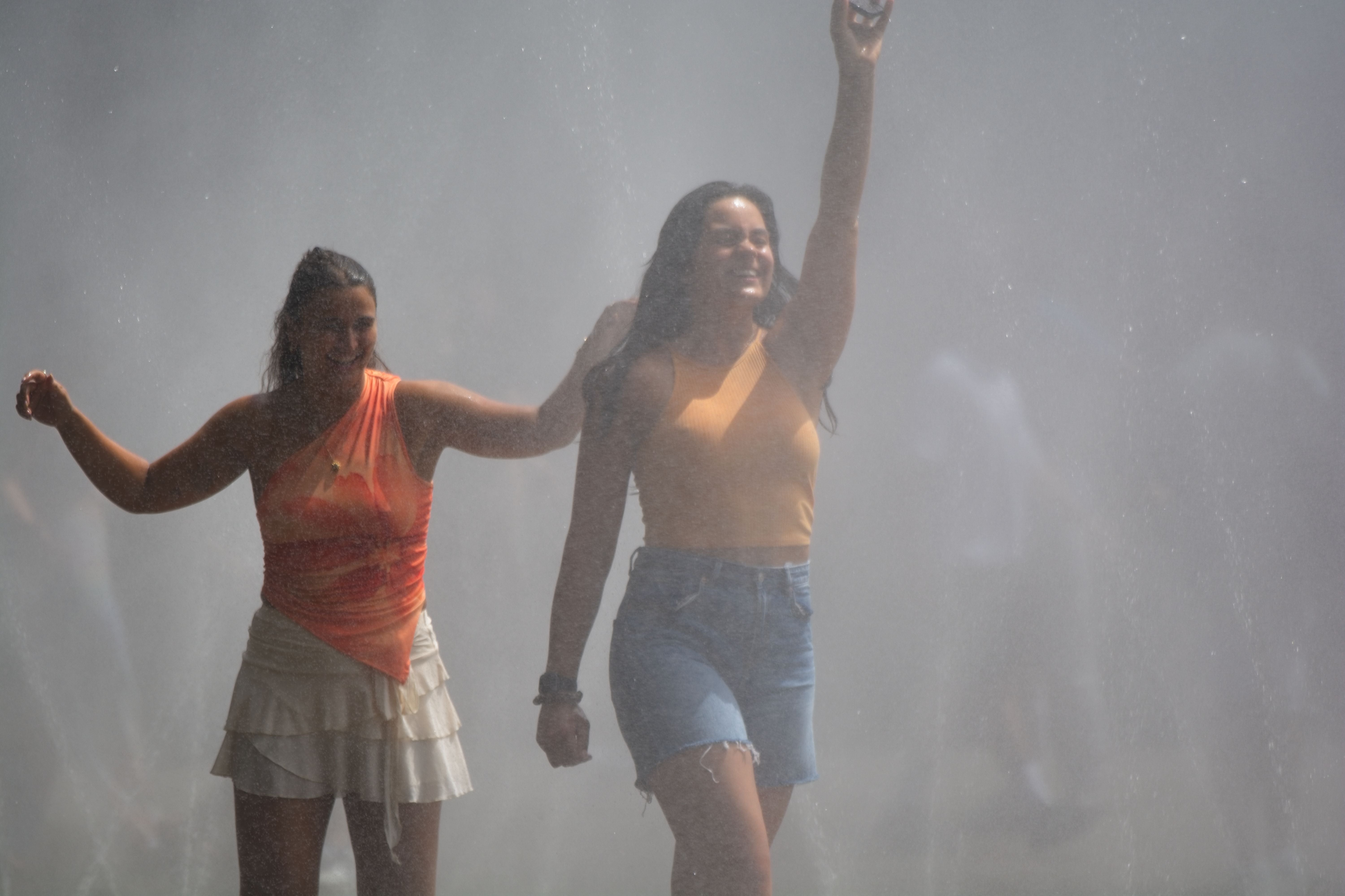 Zwei Frauen gehen durch Wassernebel in Köln an einem heißen Sommertag.