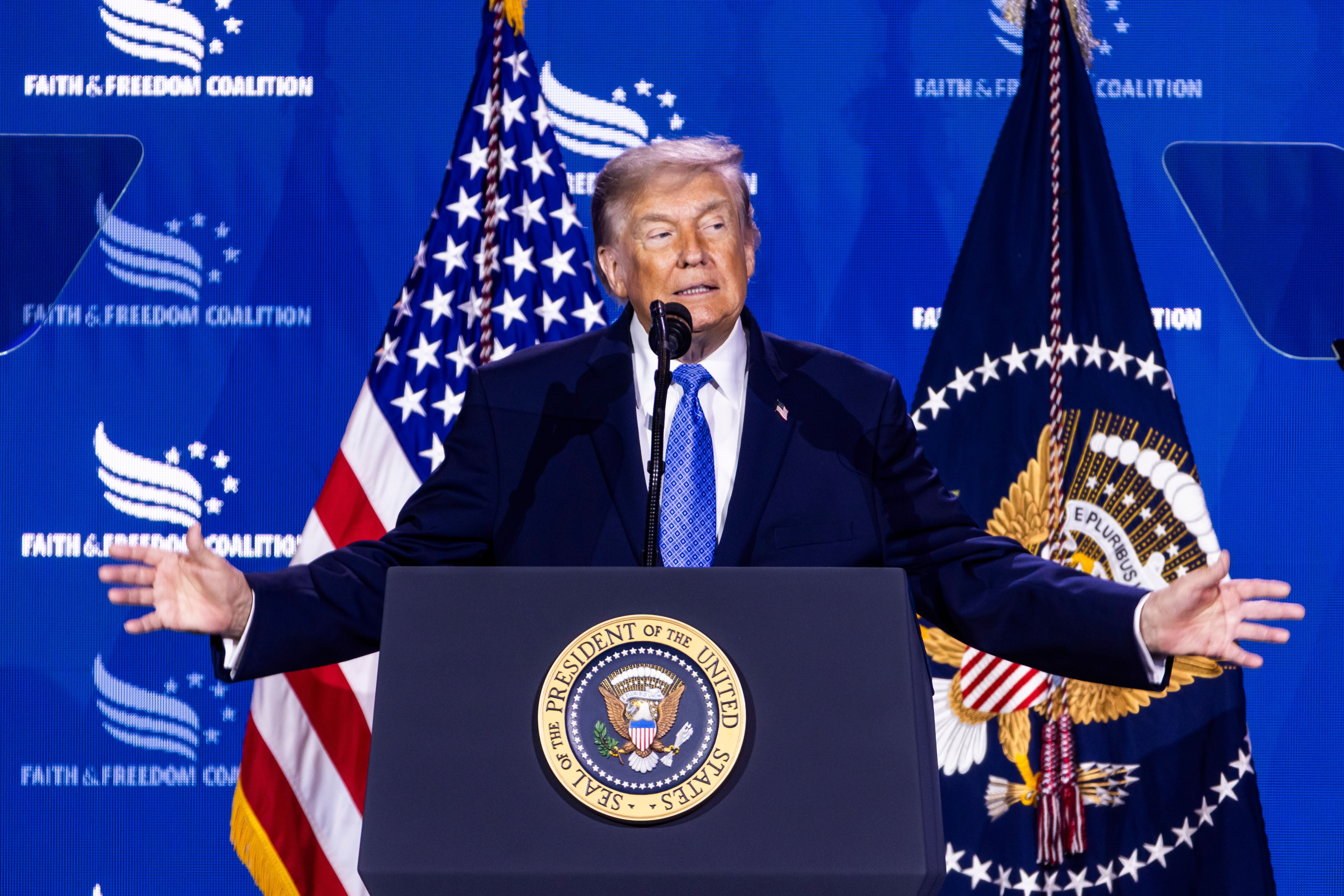 Ein Mann am Rednerpult mit Präsidentensiegel, US-Flaggen und Konferenzhintergrund.
