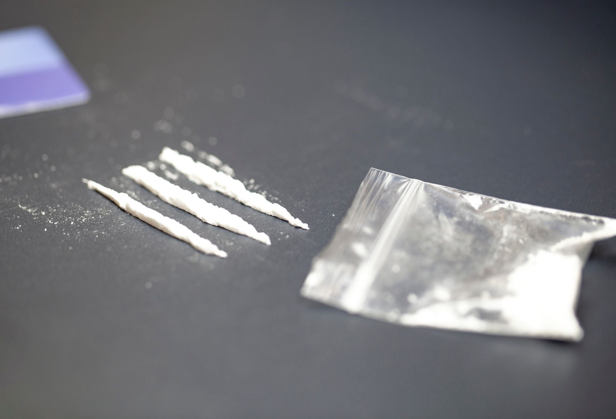 Drei Linien weißes Pulver und ein Plastiktütchen mit weißem Rückstand auf dunklem Untergrund.