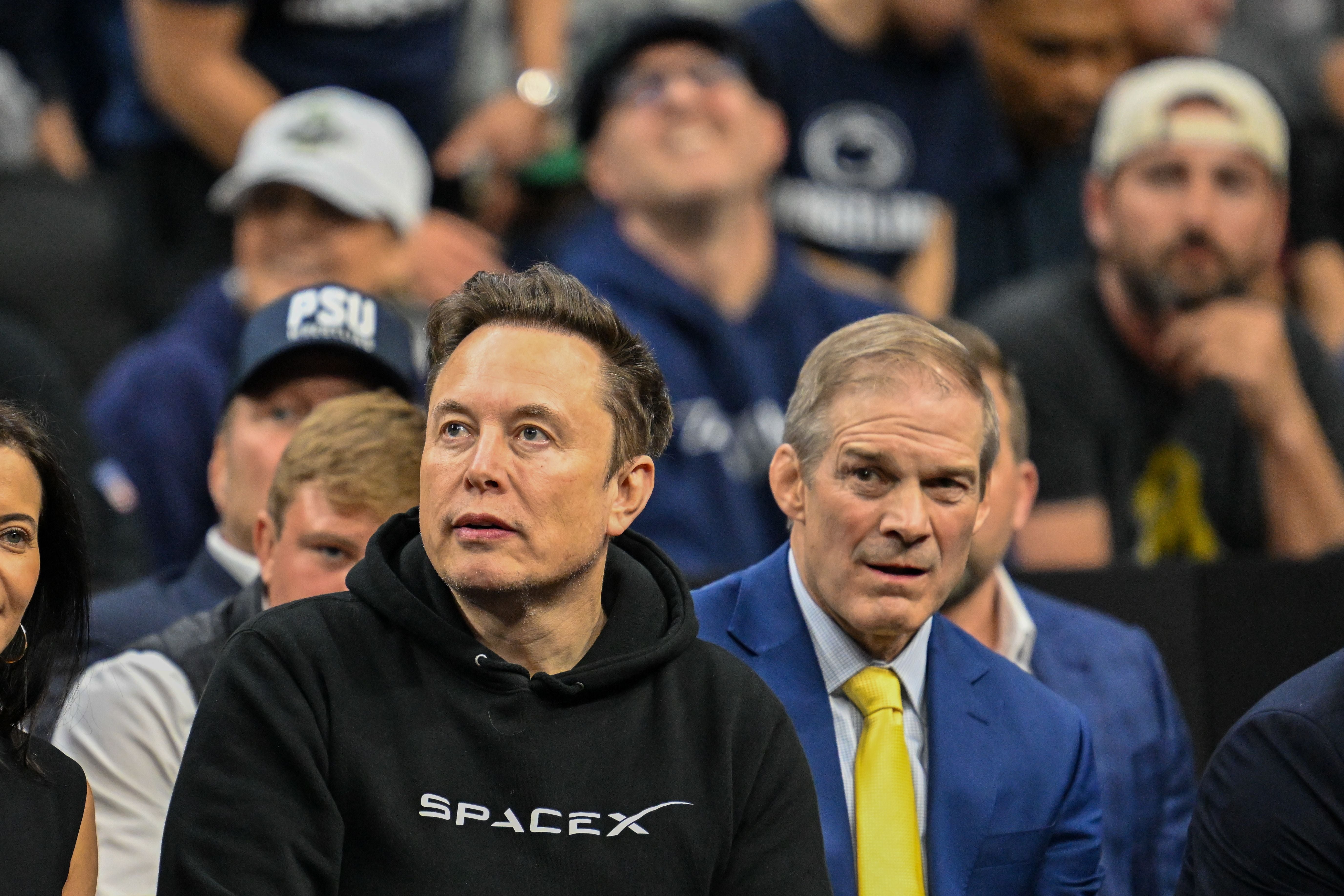 Zuschauer sitzen während eines Sportevents in einer Arena, einer trägt ein SpaceX-Hoodie.