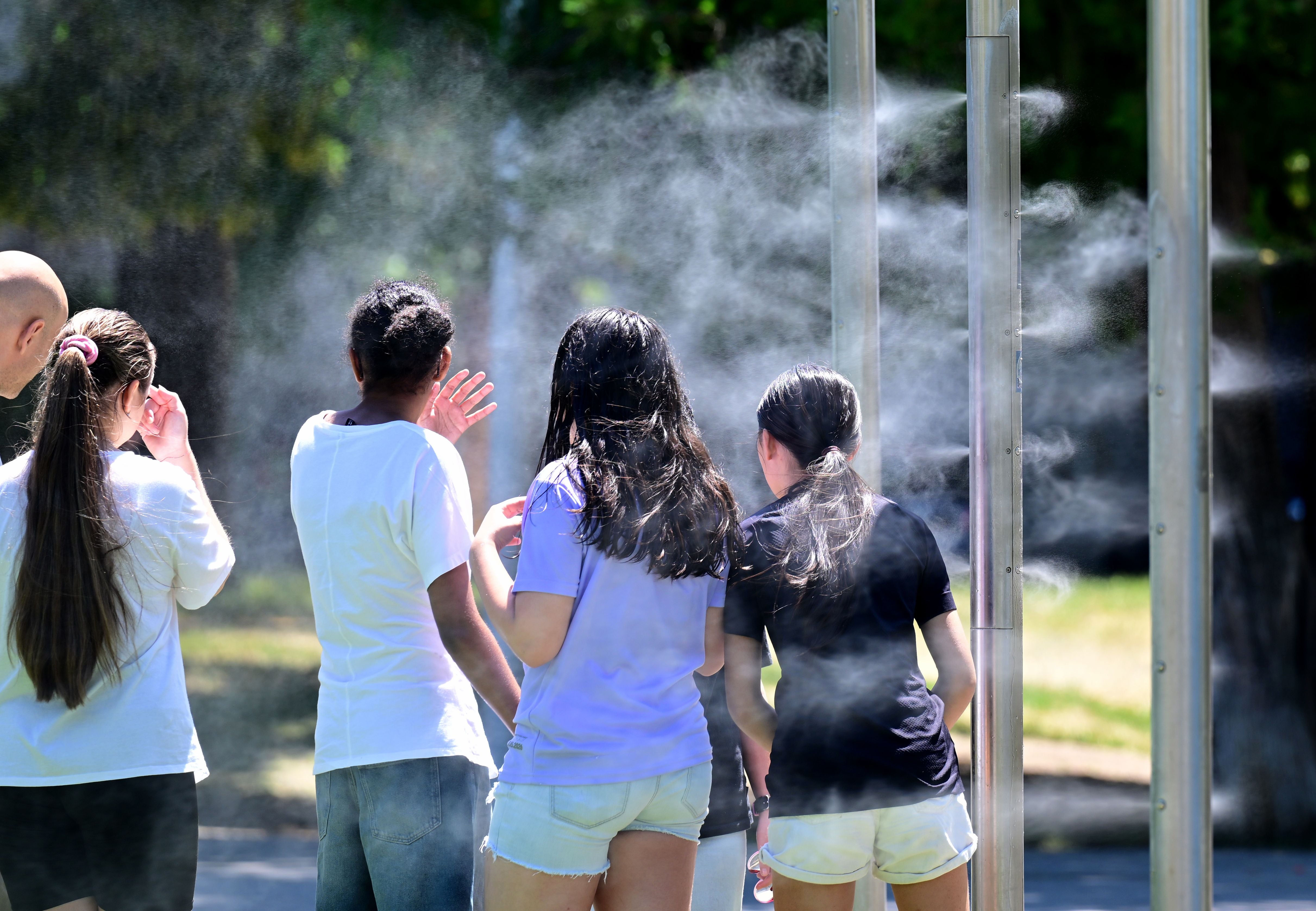 Mehrere Jugendliche kühlen sich bei Sprühnebel in einem Park an einem heißen Sommertag ab.