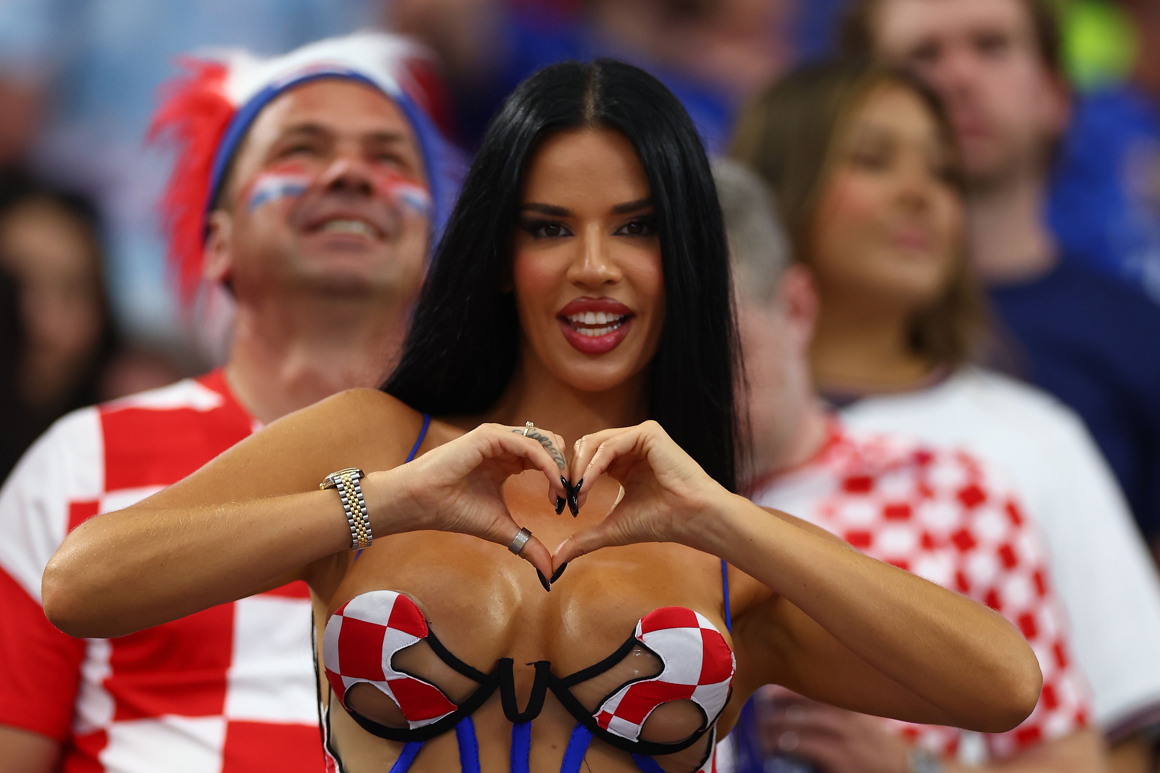 Frau im kroatischen Fan-Outfit formt ein Herz mit den Händen im Fußballstadion.
