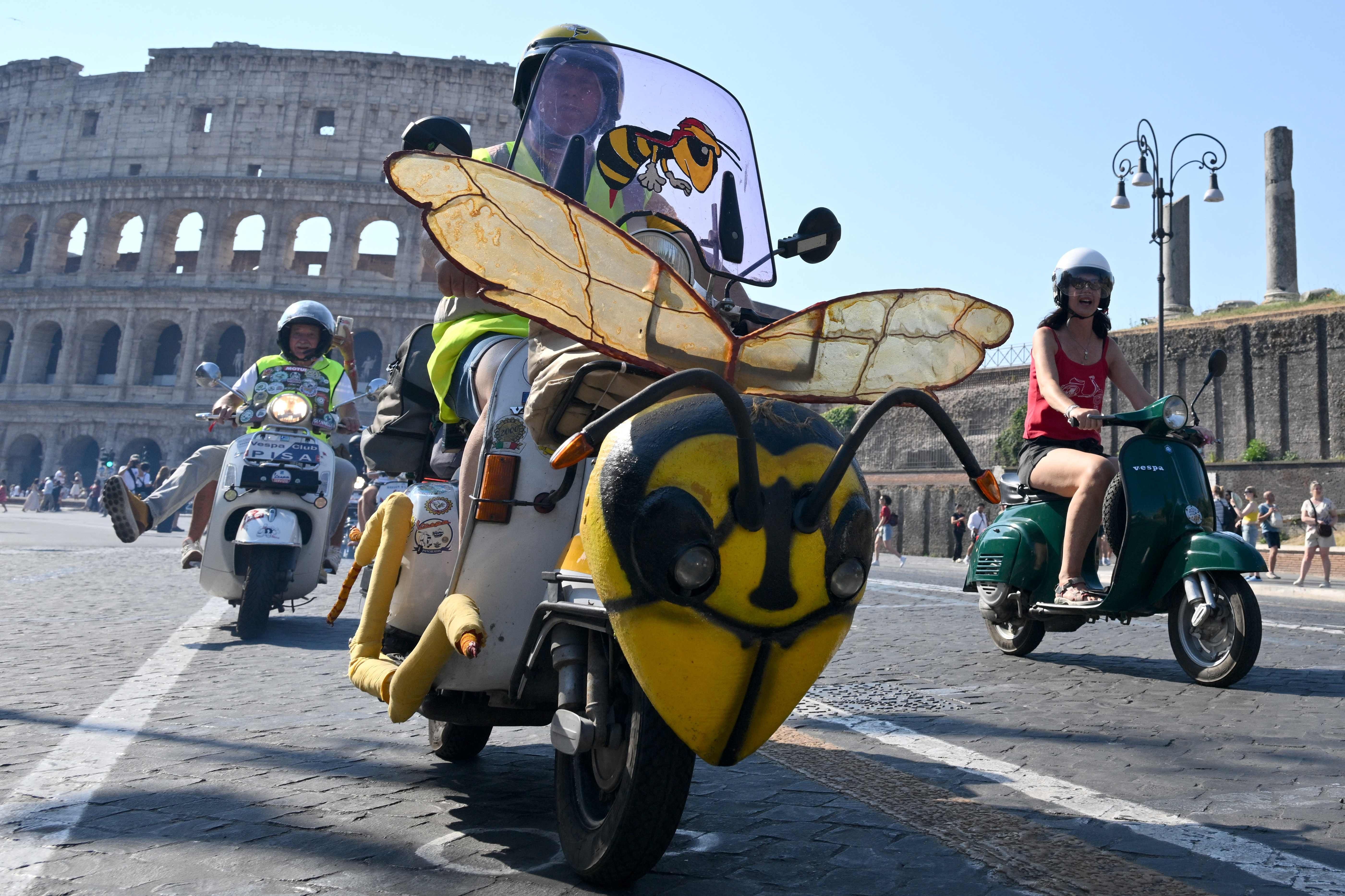 Vespa-Fahrer feiern in Rom, ein Roller ist als gelbe Wespe verkleidet, das Kolosseum im Hintergrund.