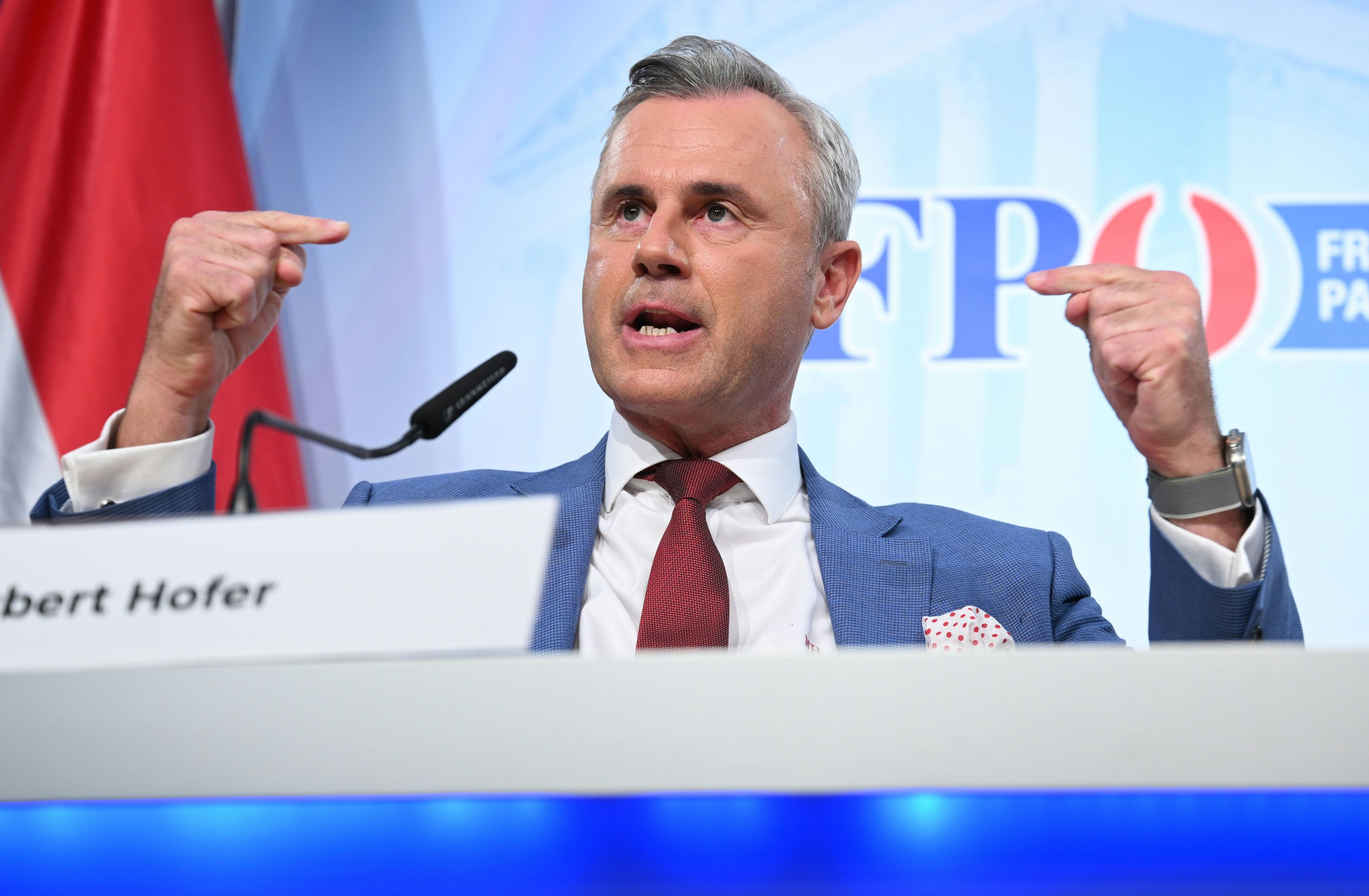 Ein Mann im Anzug spricht bei einer Pressekonferenz und gestikuliert mit beiden Händen.