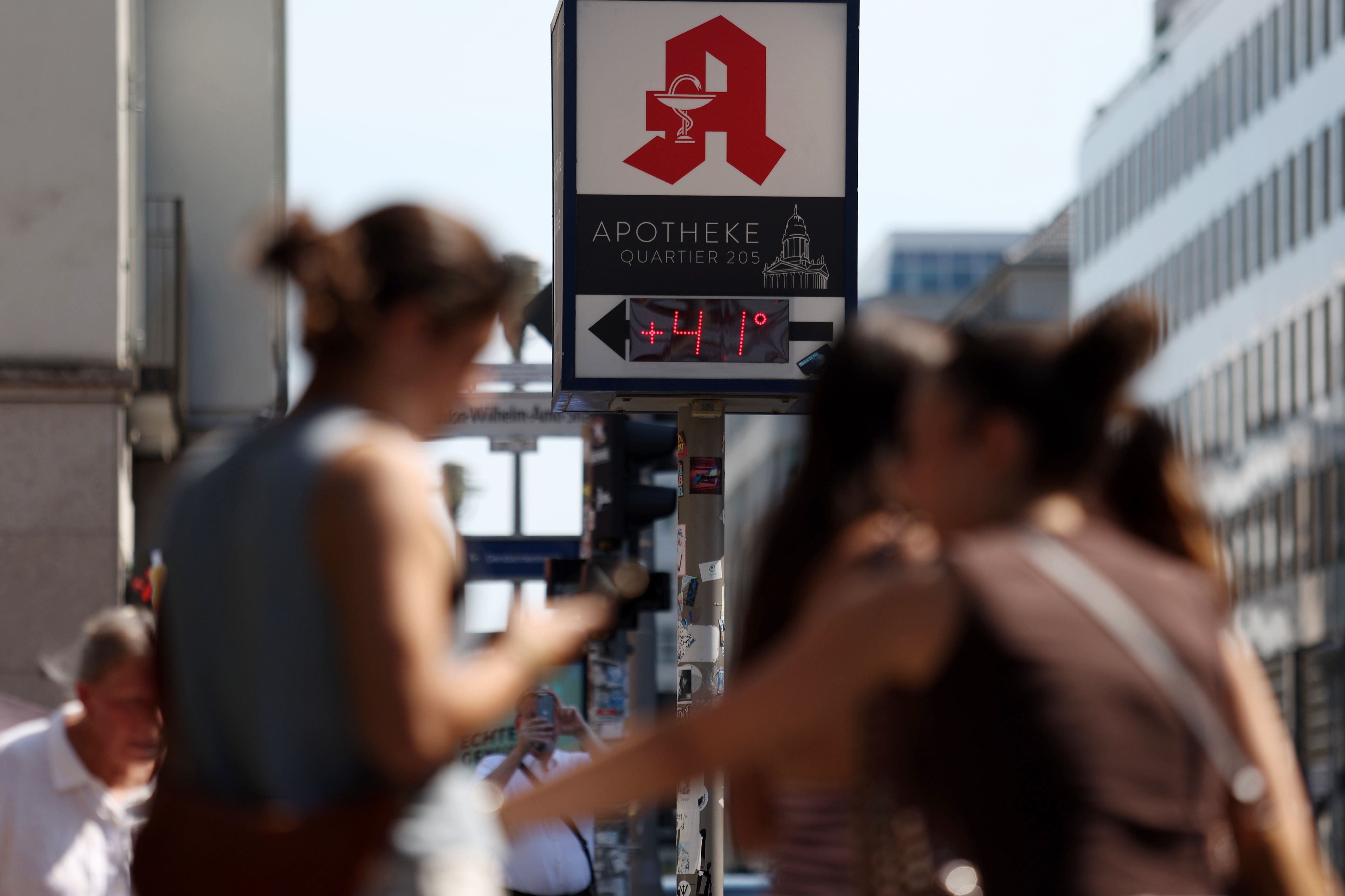 Eine Anzeige vor einer Apotheke zeigt 41 Grad Celsius, Menschen gehen in der Sommerhitze vorbei.