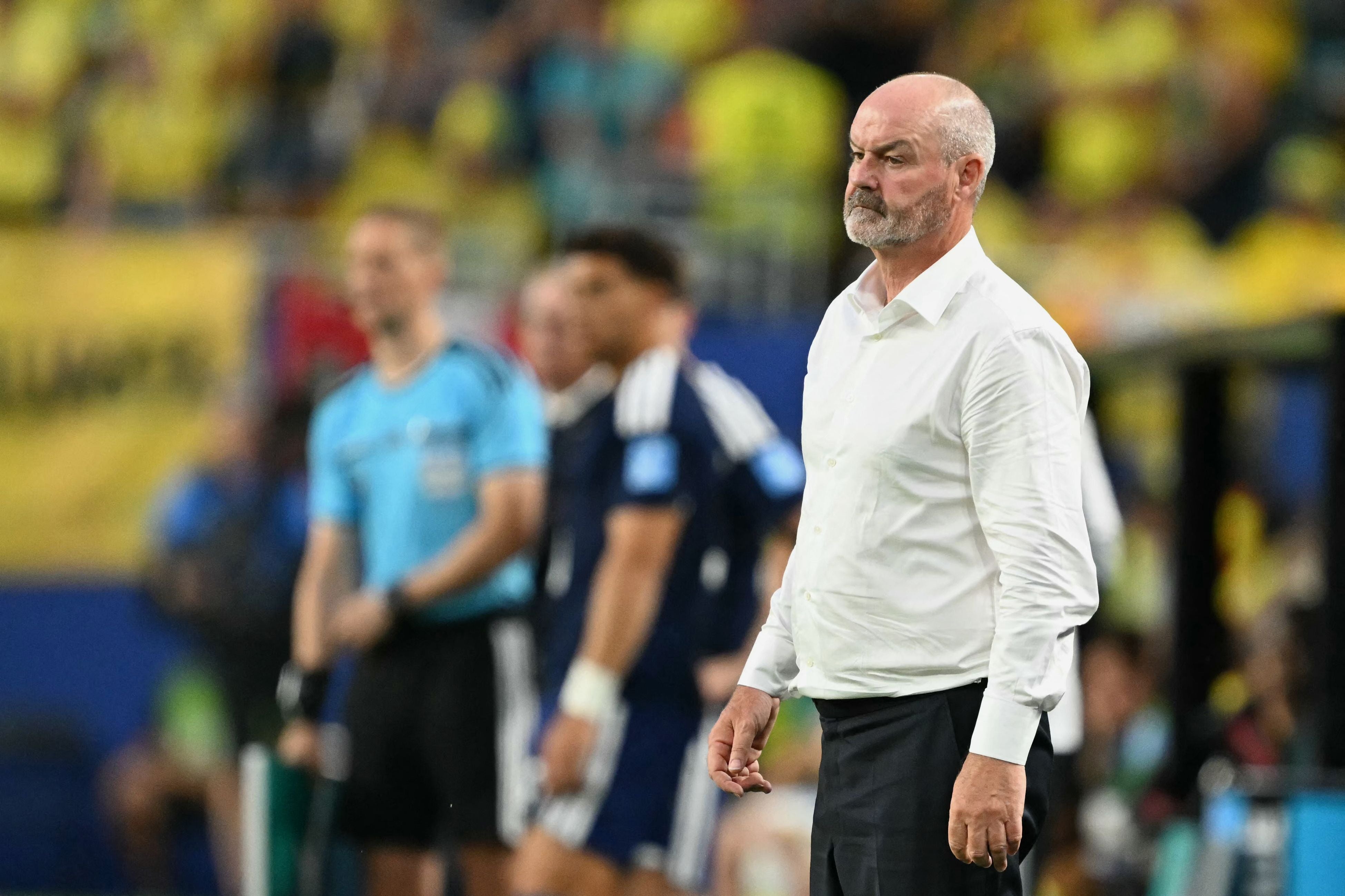 Ein Fußballtrainer im weißen Hemd steht am Spielfeldrand und blickt konzentriert.