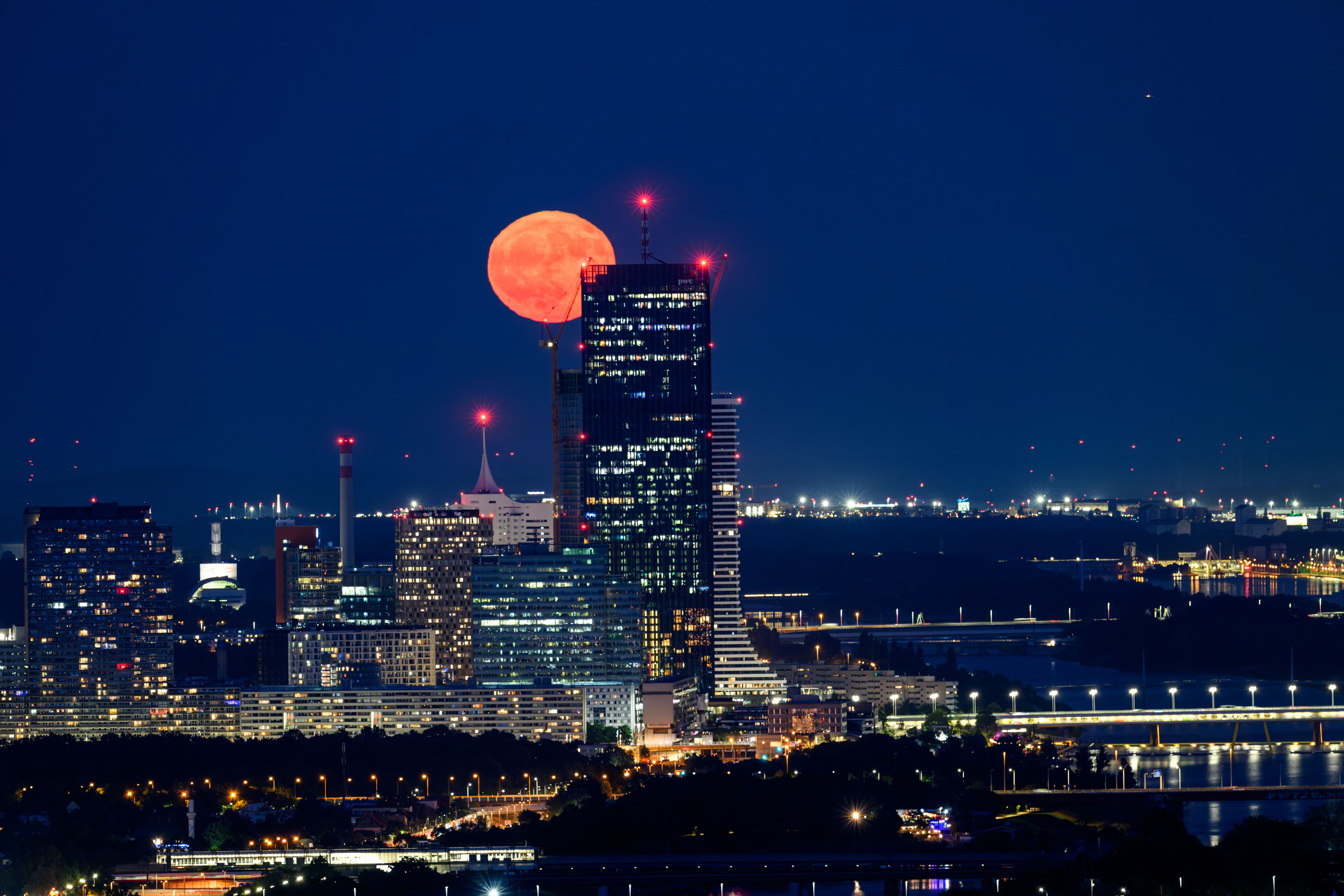 Ein großer, rot gefärbter Vollmond steht nachts über der Wiener Skyline.