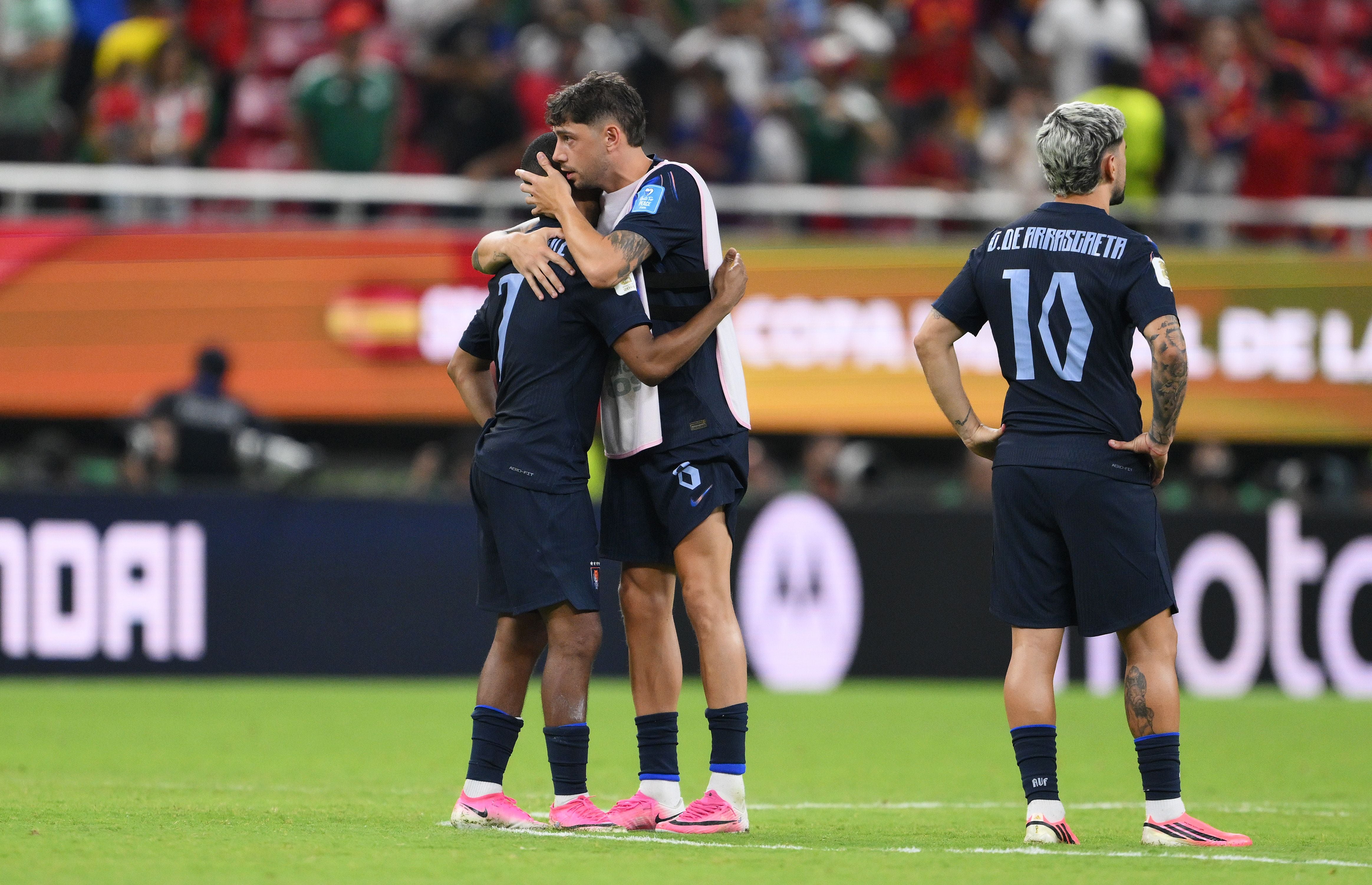 Zwei uruguayische Fußballspieler umarmen sich traurig nach einer Niederlage, ein dritter steht daneben.