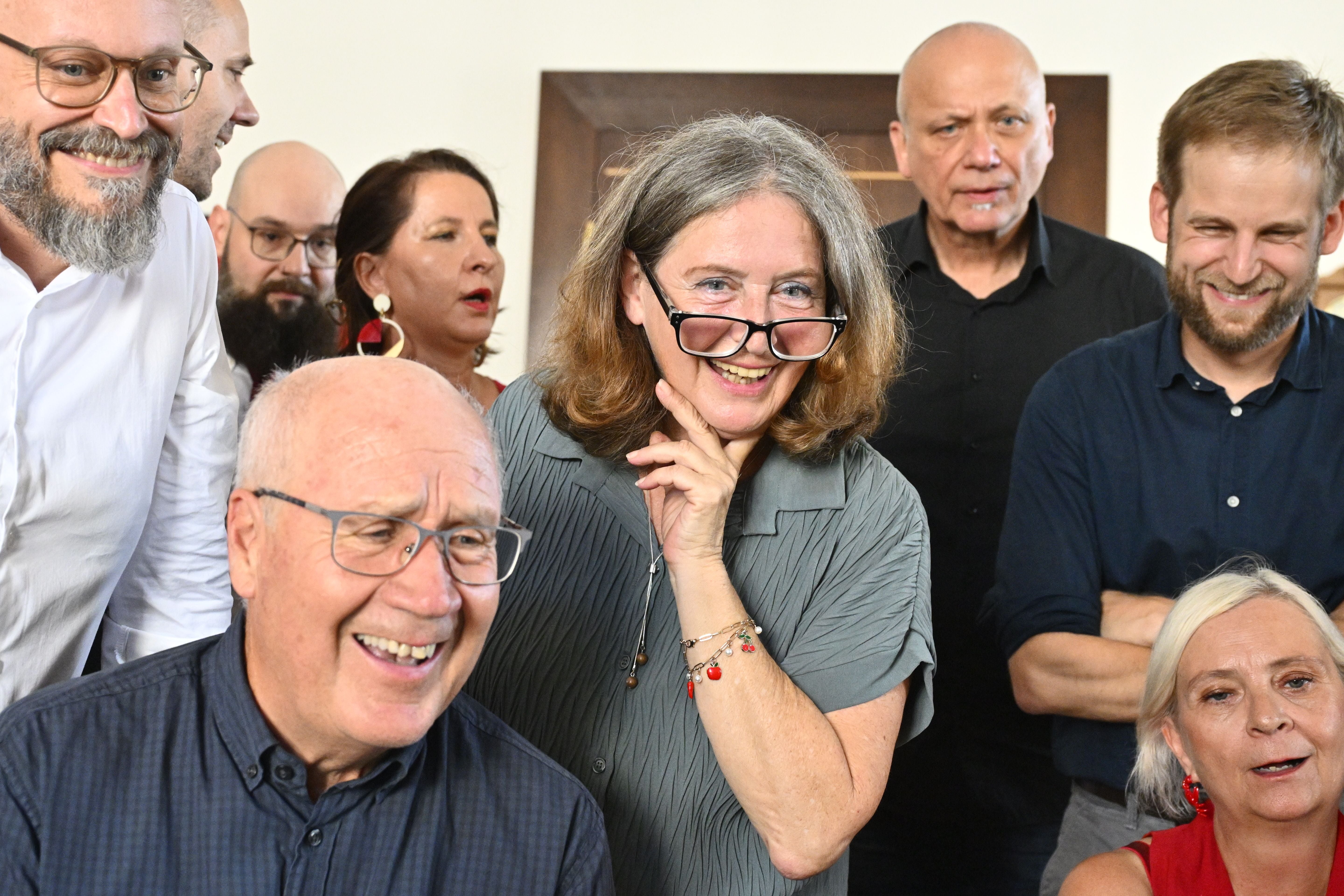 Mehrere Menschen, teils lachend, verfolgen gespannt die Präsentation eines Wahlergebnisses.