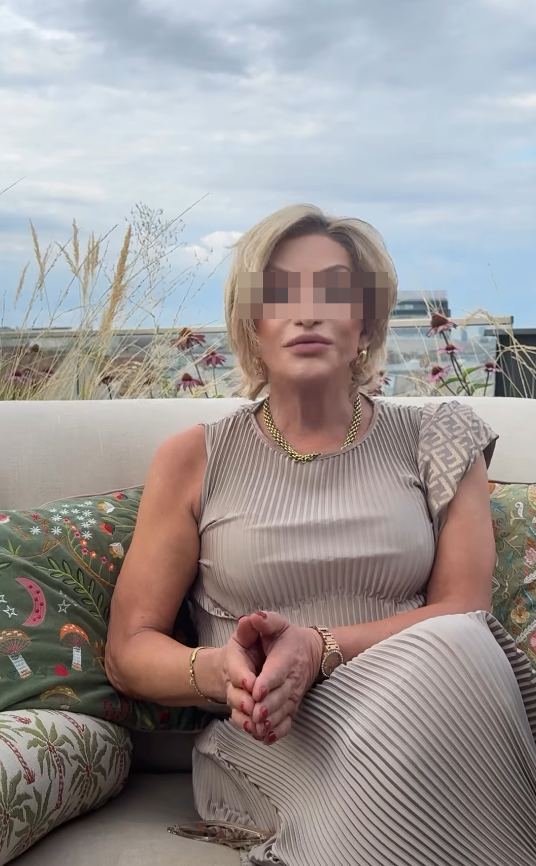 Ältere Frau sitzt auf einem Sofa im Freien, umgeben von Pflanzen und bunten Kissen.