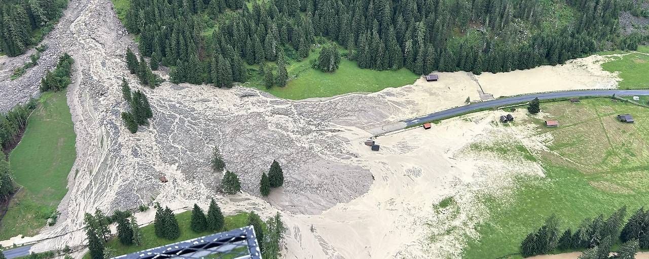 Großer Murenabgang überquert eine Straße in einer bewaldeten Gebirgslandschaft.