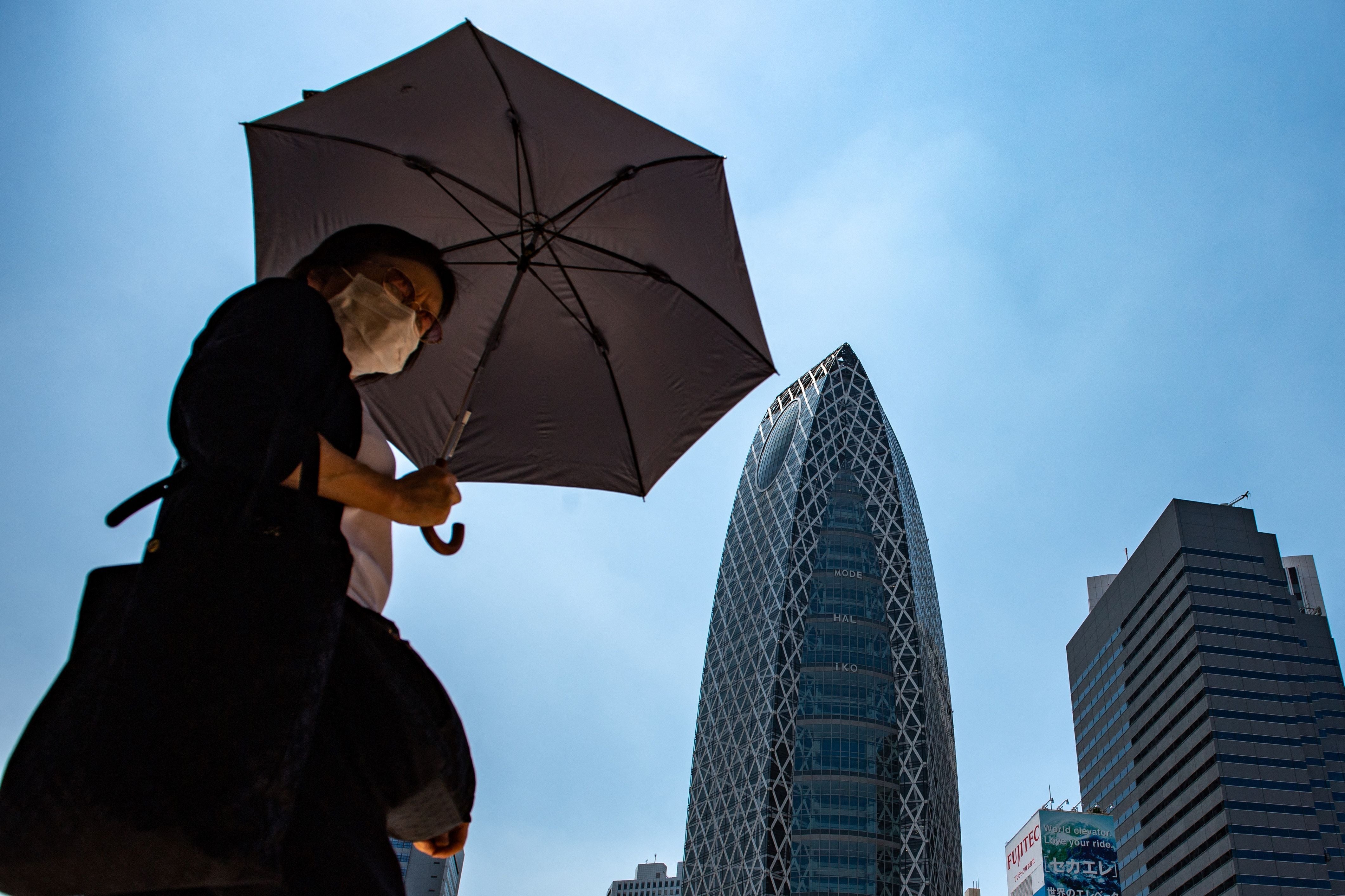 Eine Person geht mit einem Regenschirm als Sonnenschutz durch Tokios Stadtteil Shinjuku.