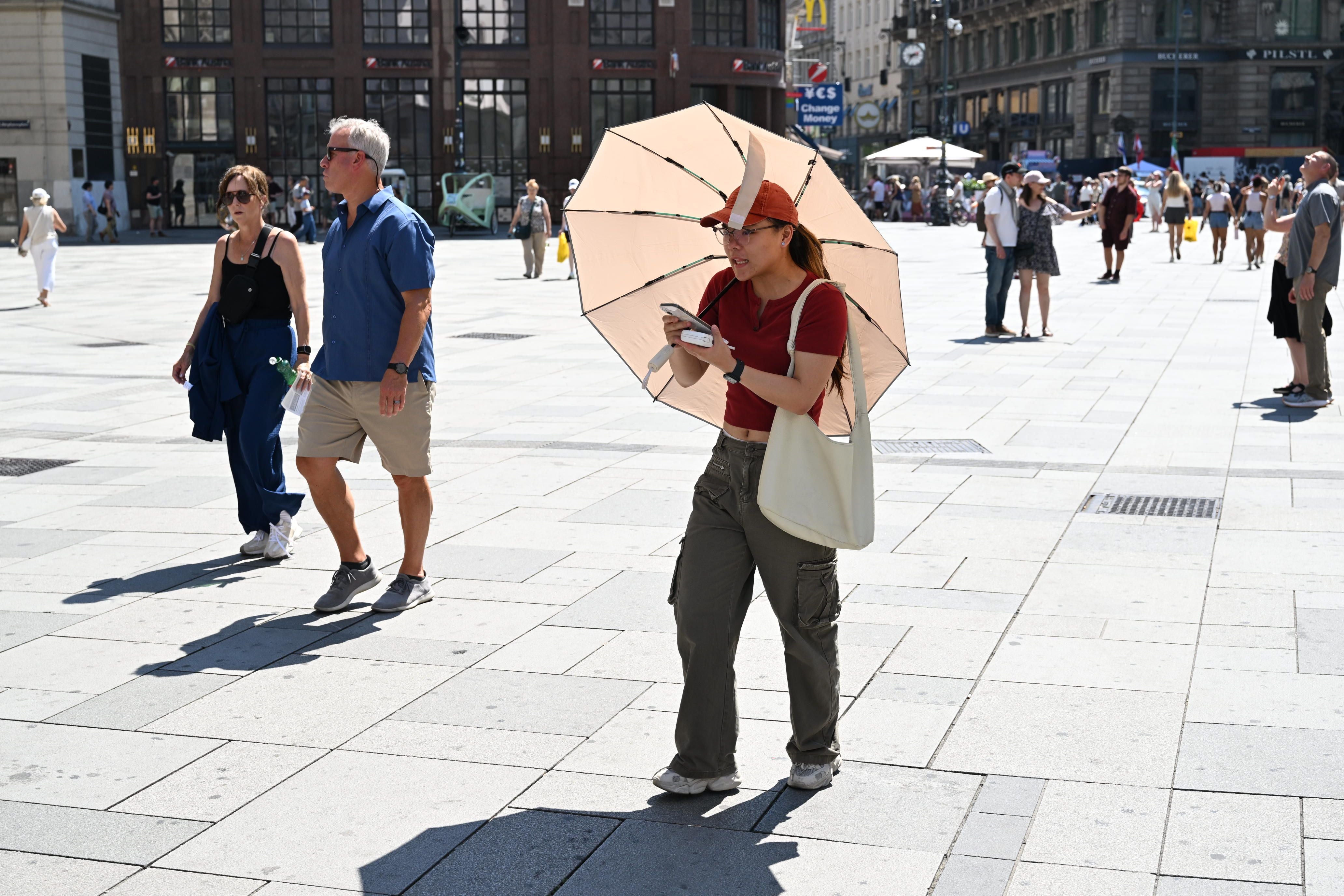 Frau mit Sonnenschirm und Handy läuft an sonnigem Tag durch die Stadt.