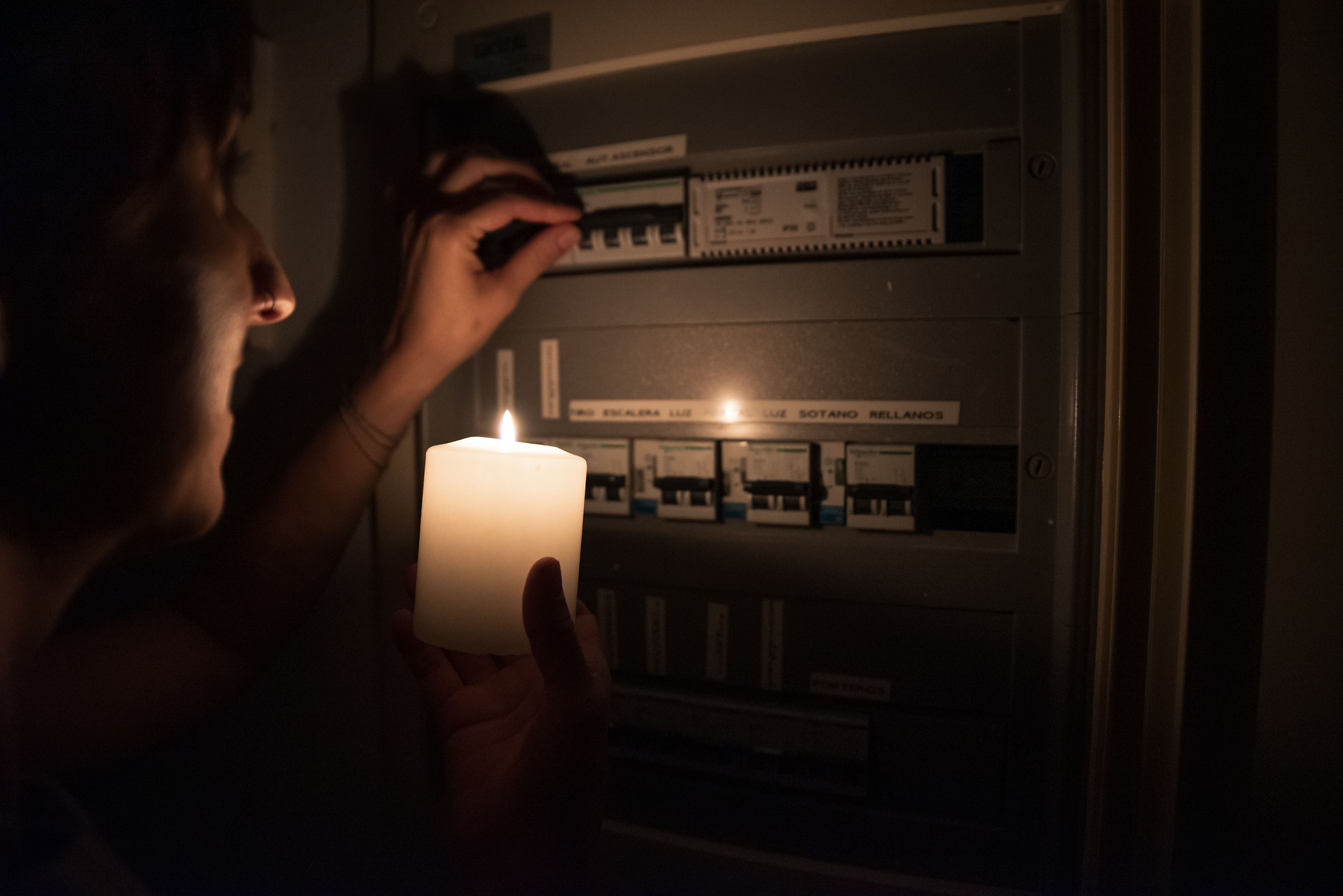 Frau hält eine Kerze und prüft bei Stromausfall einen Sicherungskasten.