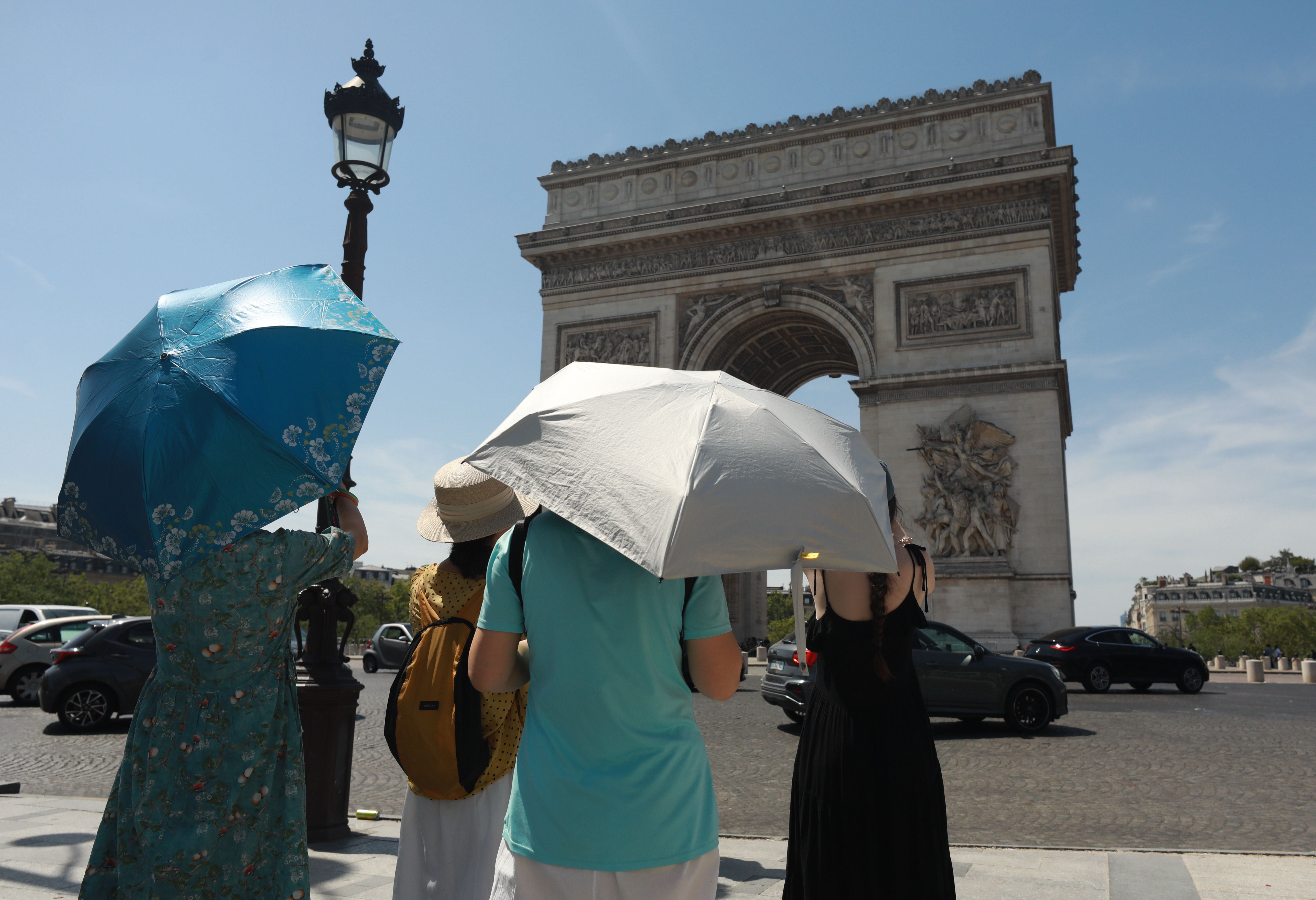 Touristen mit Sonnenschirmen vor dem Arc de Triomphe an einem heißen Tag in Paris.