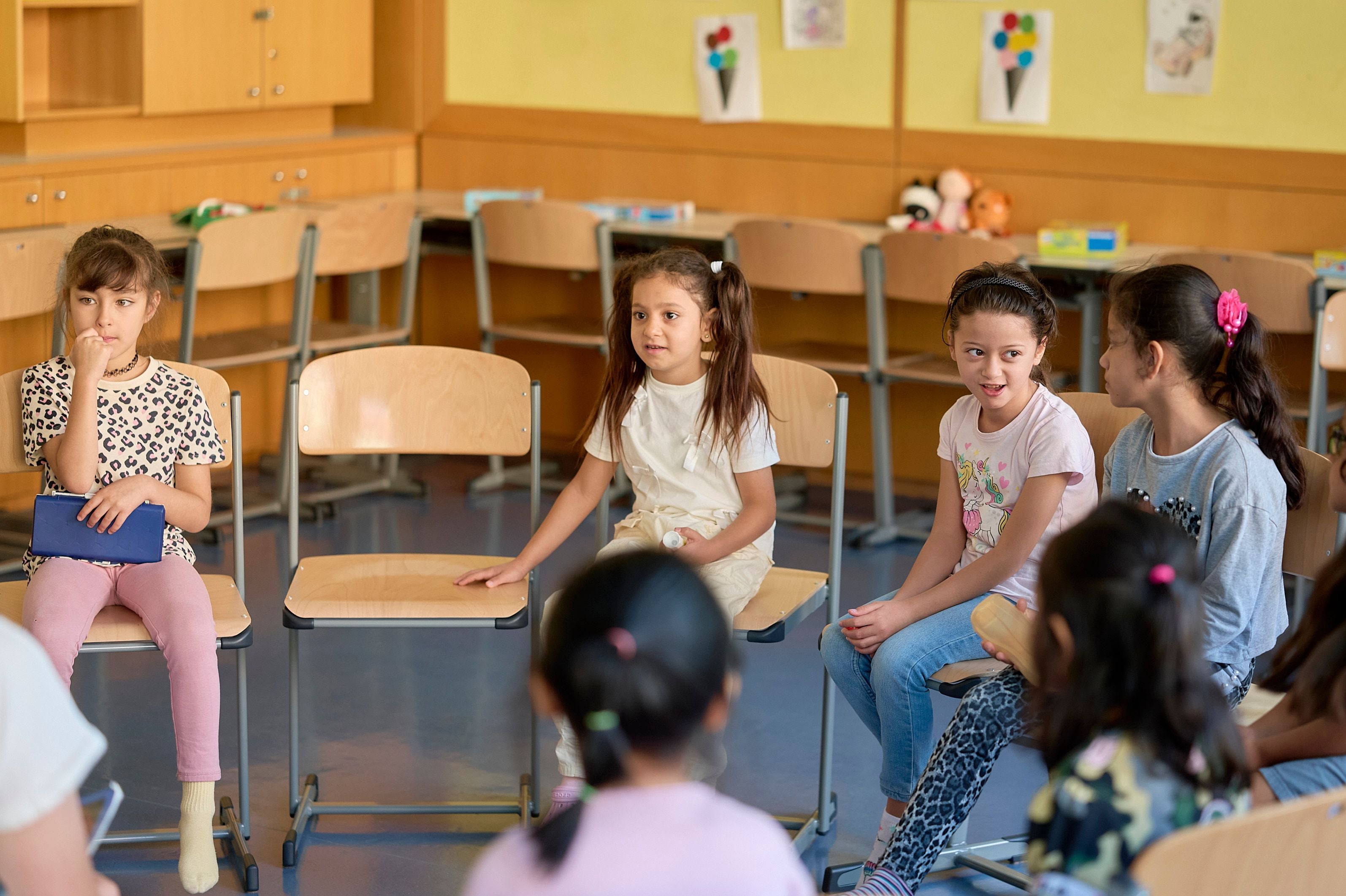 Mehrere Kinder sitzen im Stuhlkreis in einem Klassenraum und unterhalten sich.