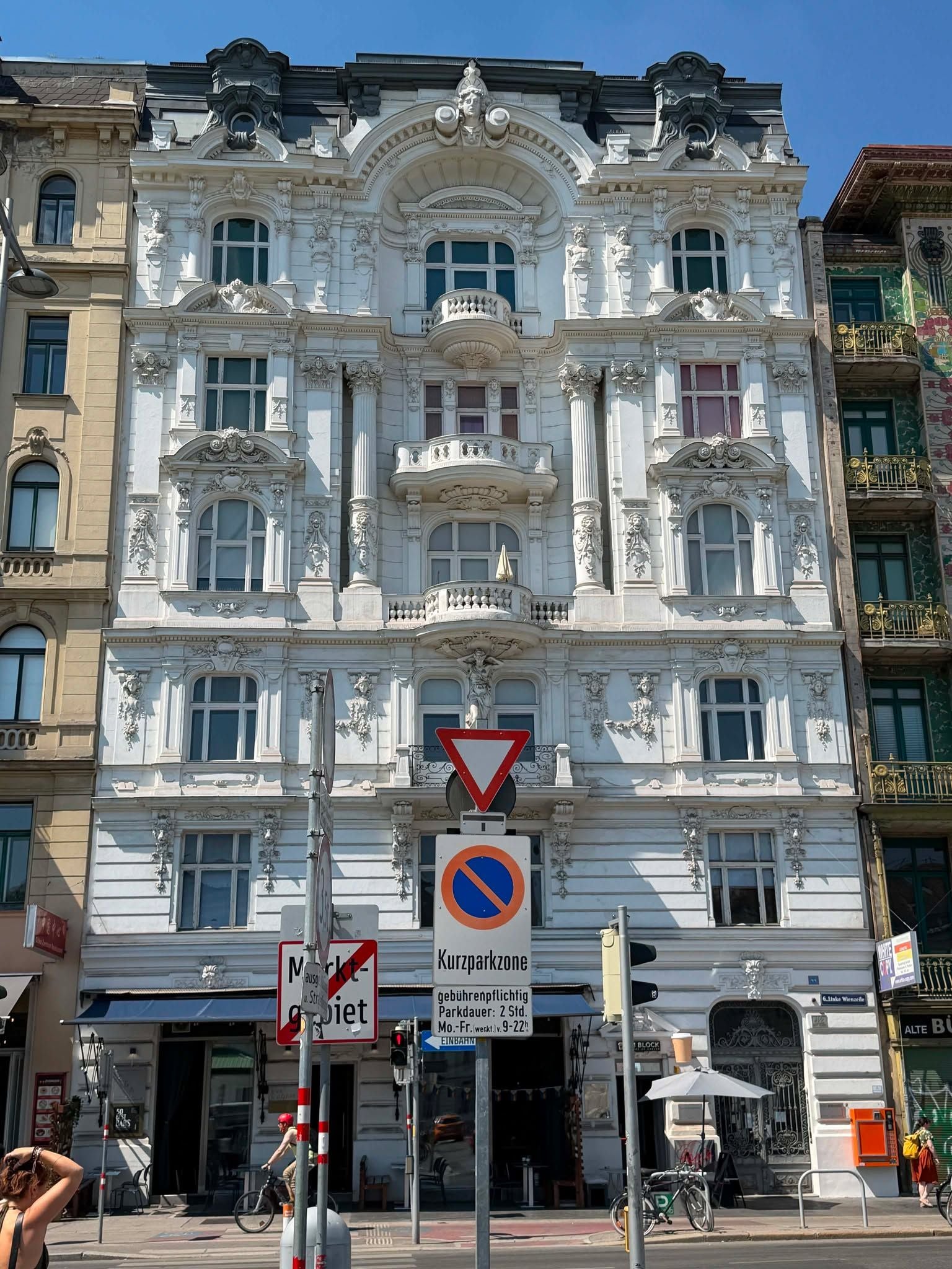 Prunkvolle weiße Jugendstil-Fassade mit Erkern und Balkonen, Straßenschilder im Vordergrund.