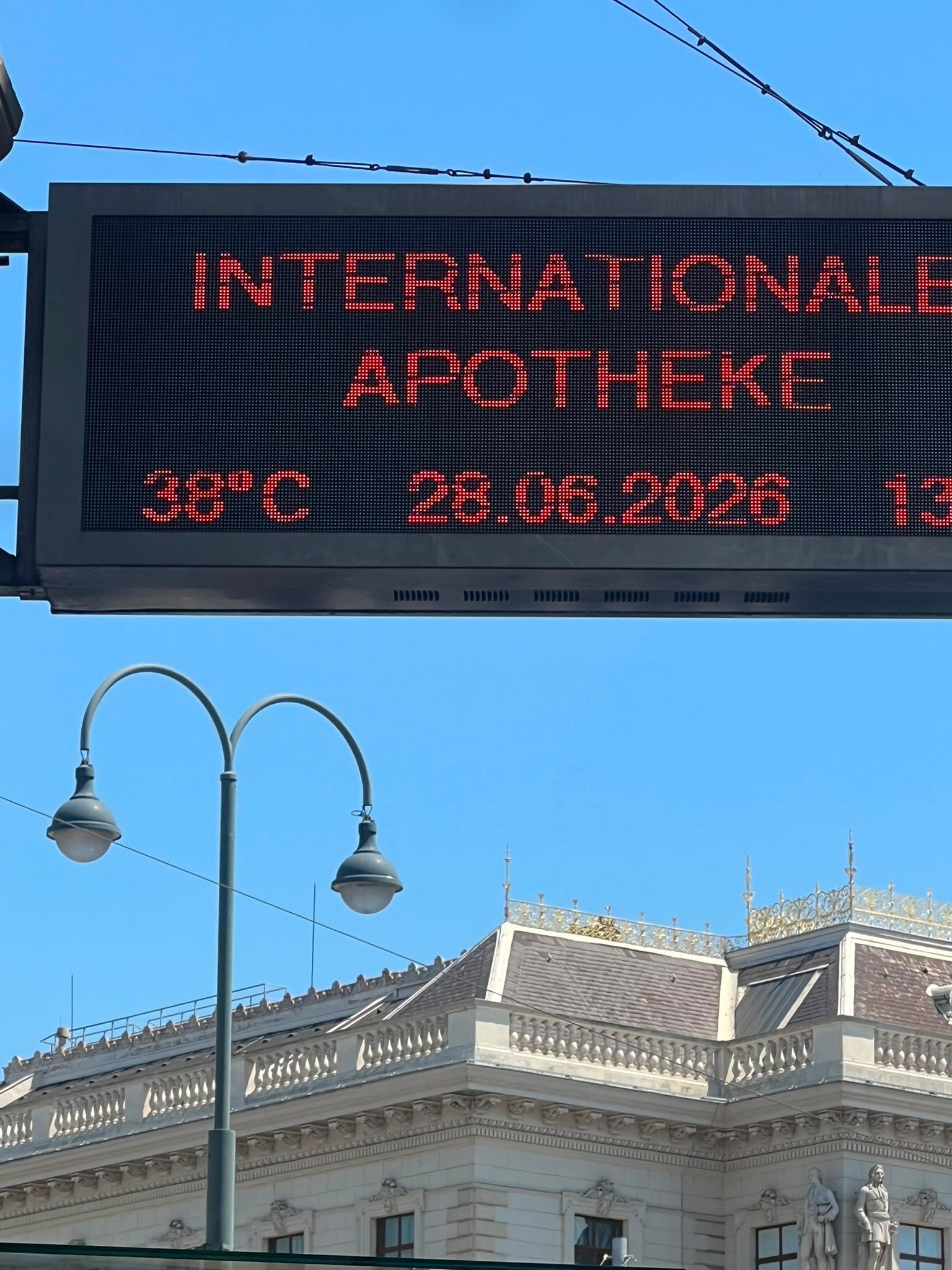 Digitale Anzeige in Wien zeigt 38°C und das Datum 28.06.2026 vor historischer Gebäudeansicht.