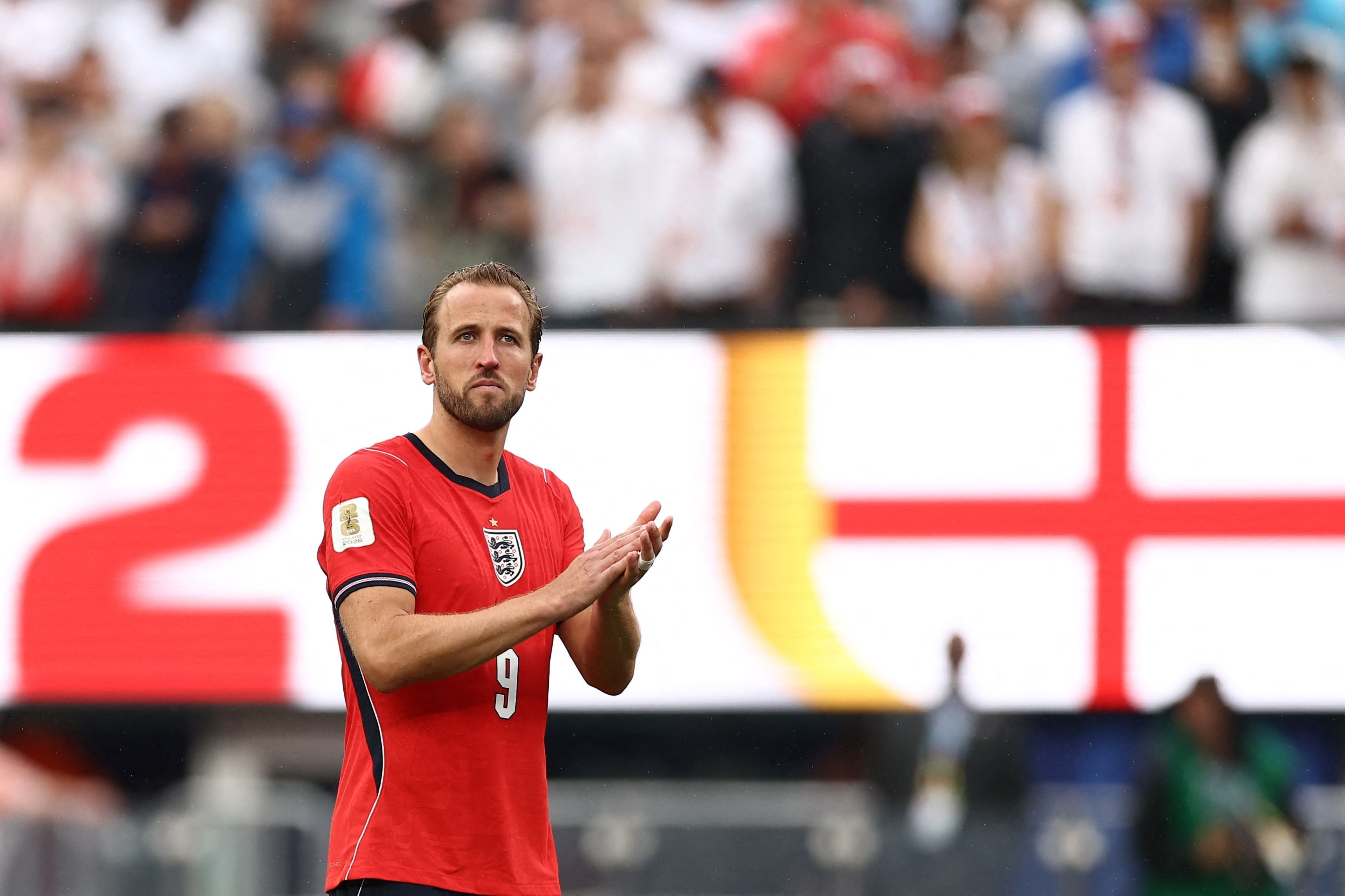 Ein englischer Fußballspieler im roten Trikot klatscht vor einer Menschenmenge im Stadion.