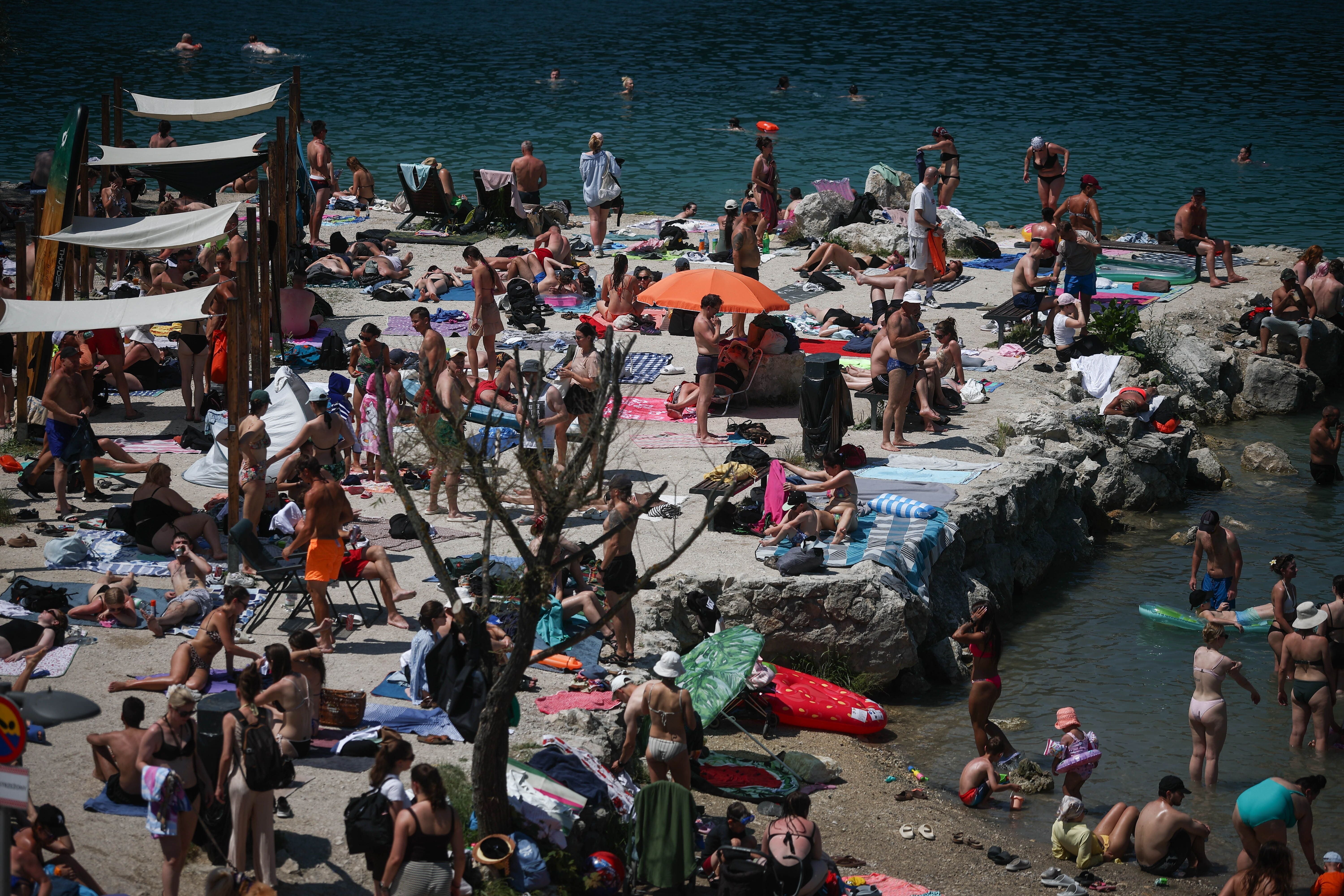 Viele Menschen entspannen und schwimmen an einem belebten Felsenstrand am Wasser bei Sonnenschein.