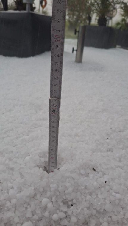 Ein Zollstock misst etwa 20 cm Höhe von dichtem Hagel bedecktem Boden.