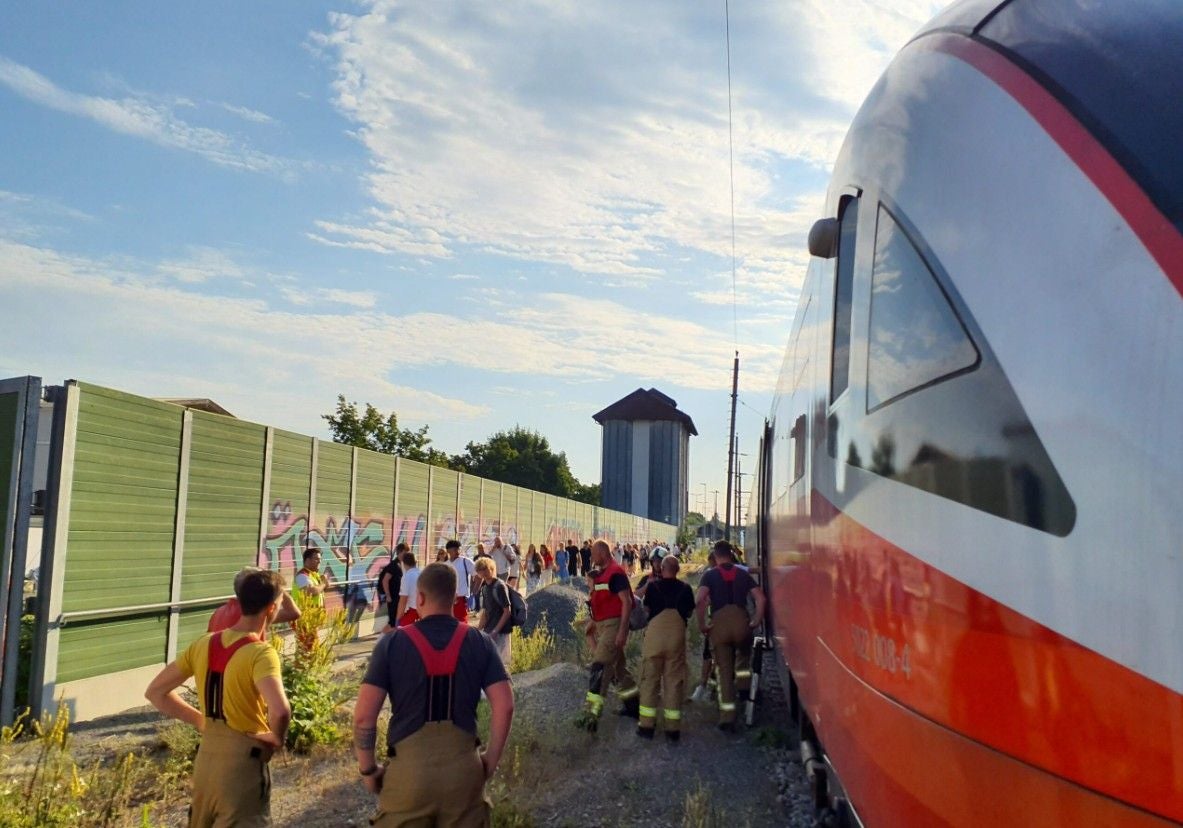 Feuerwehr evakuiert viele Menschen aus einem defekten Zug neben einer Lärmschutzwand.