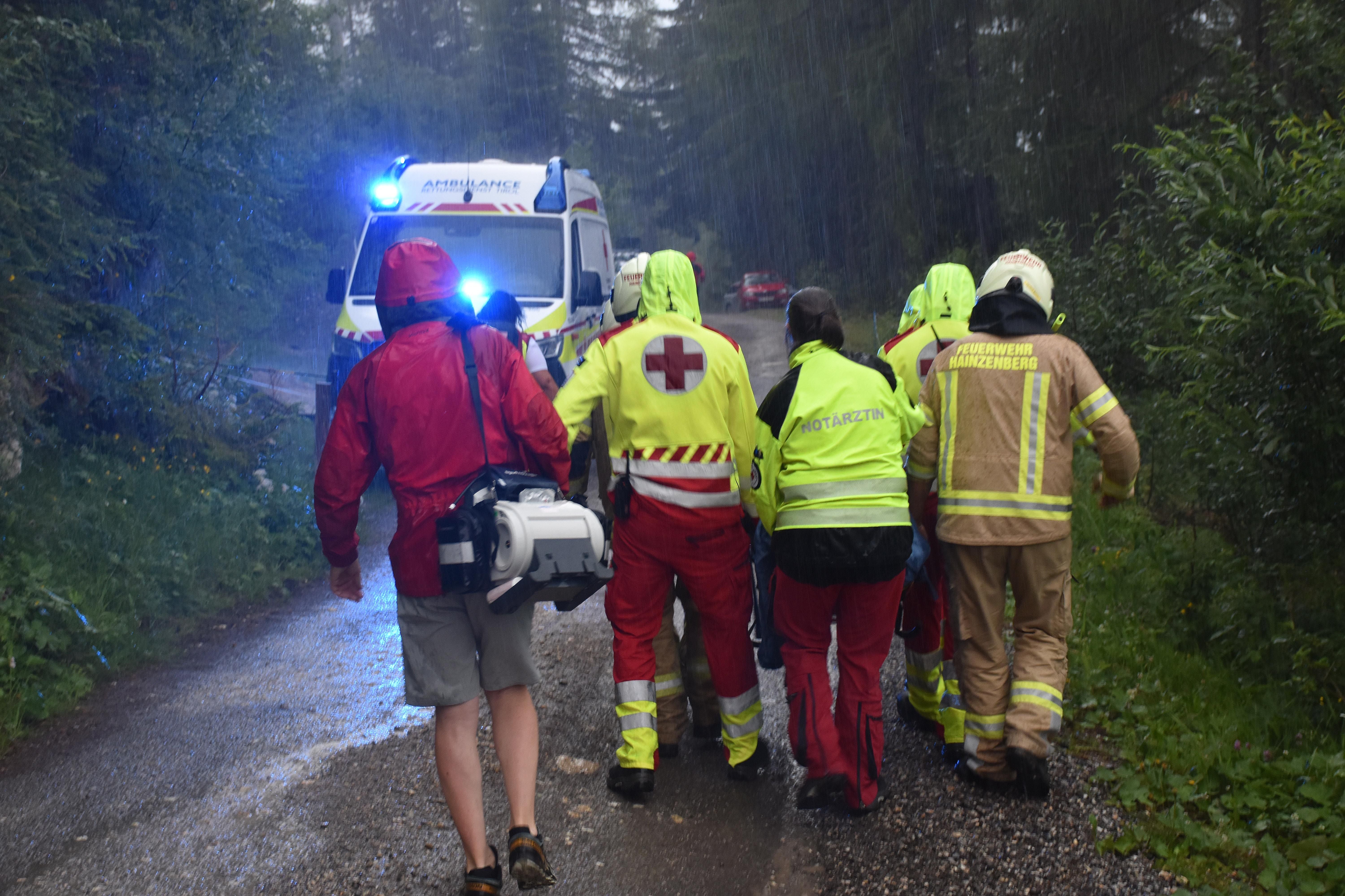 Rettungskräfte begleiten bei Regen eine Person auf einer Trage zu einem Krankenwagen im Wald.