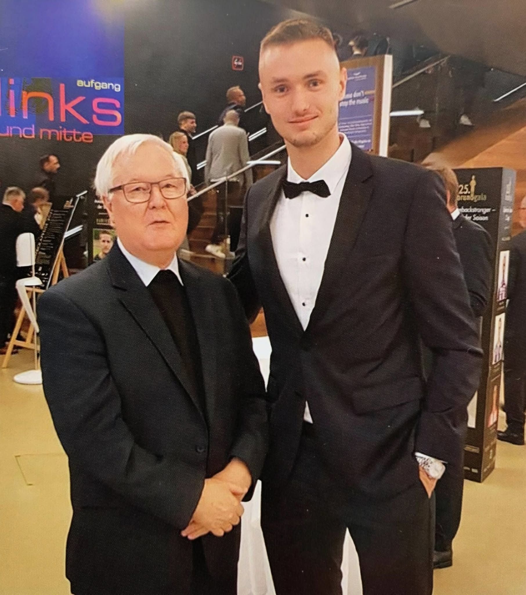 Zwei Männer im Anzug posieren für ein Foto bei einer festlichen Veranstaltung.