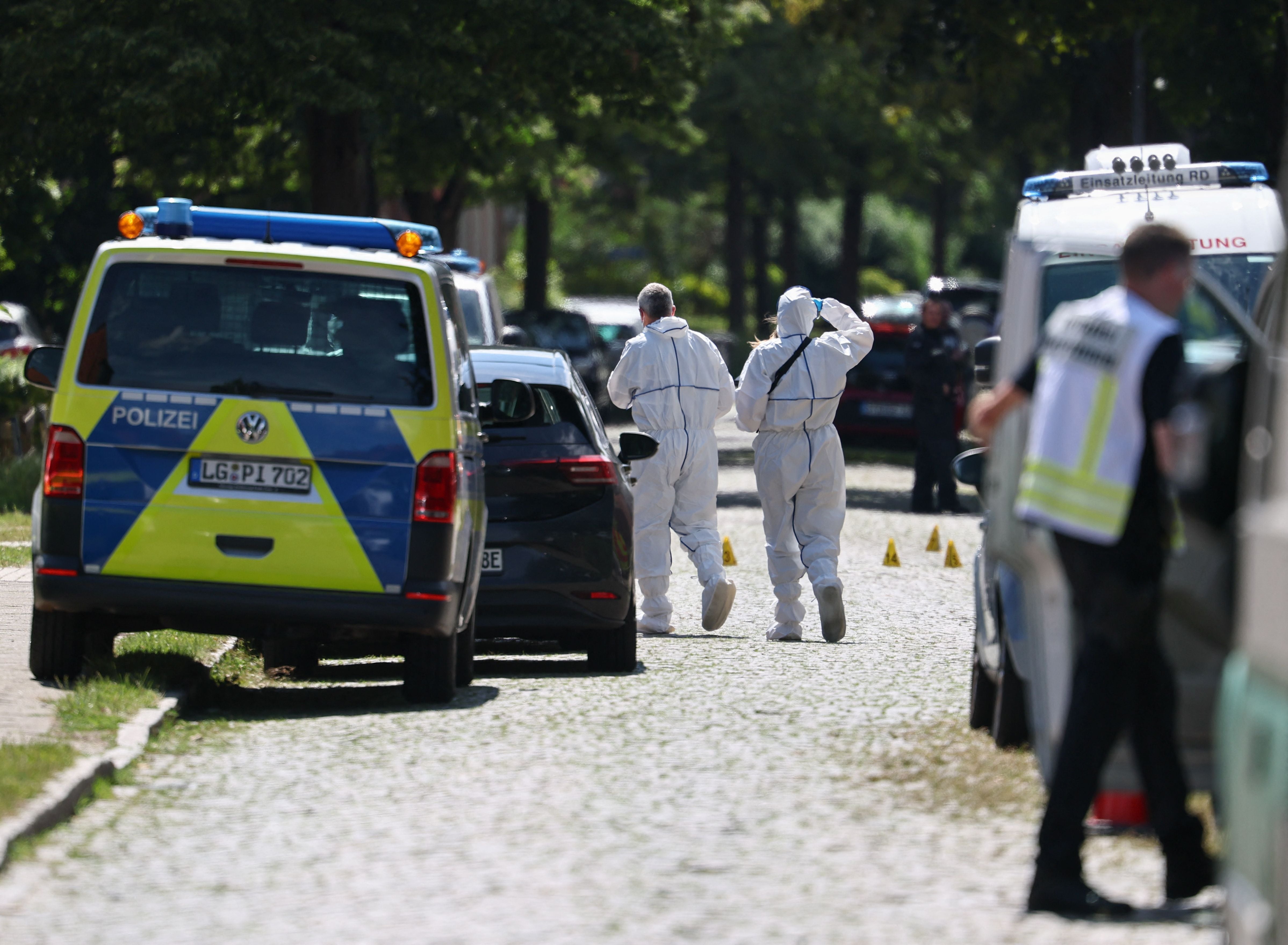 Polizisten und Spurensicherung in Schutzanzügen arbeiten an einem abgesperrten Tatort mit Einsatzfahrzeugen.