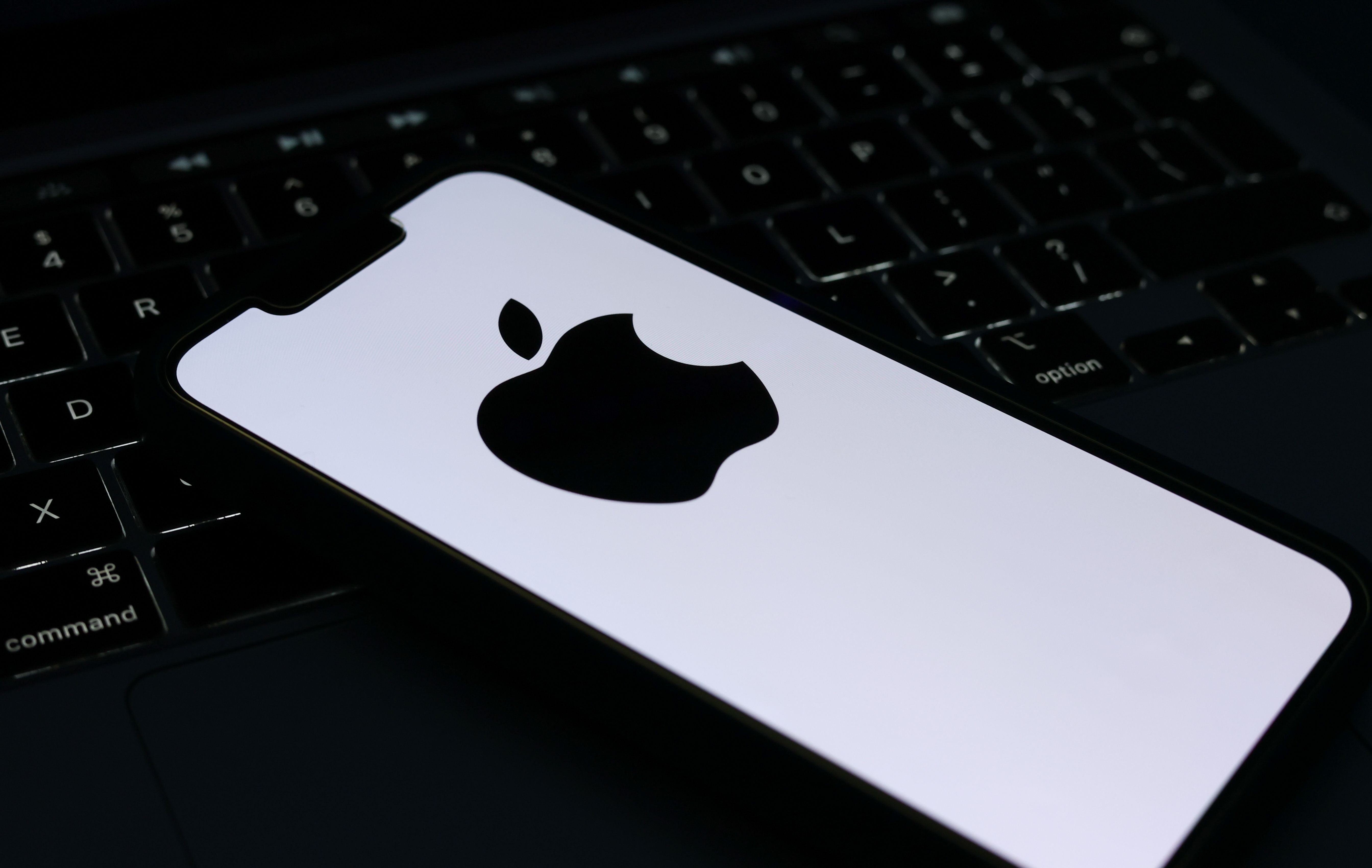 Ein Smartphone mit Apple-Logo liegt auf einer Tastatur eines Laptops.